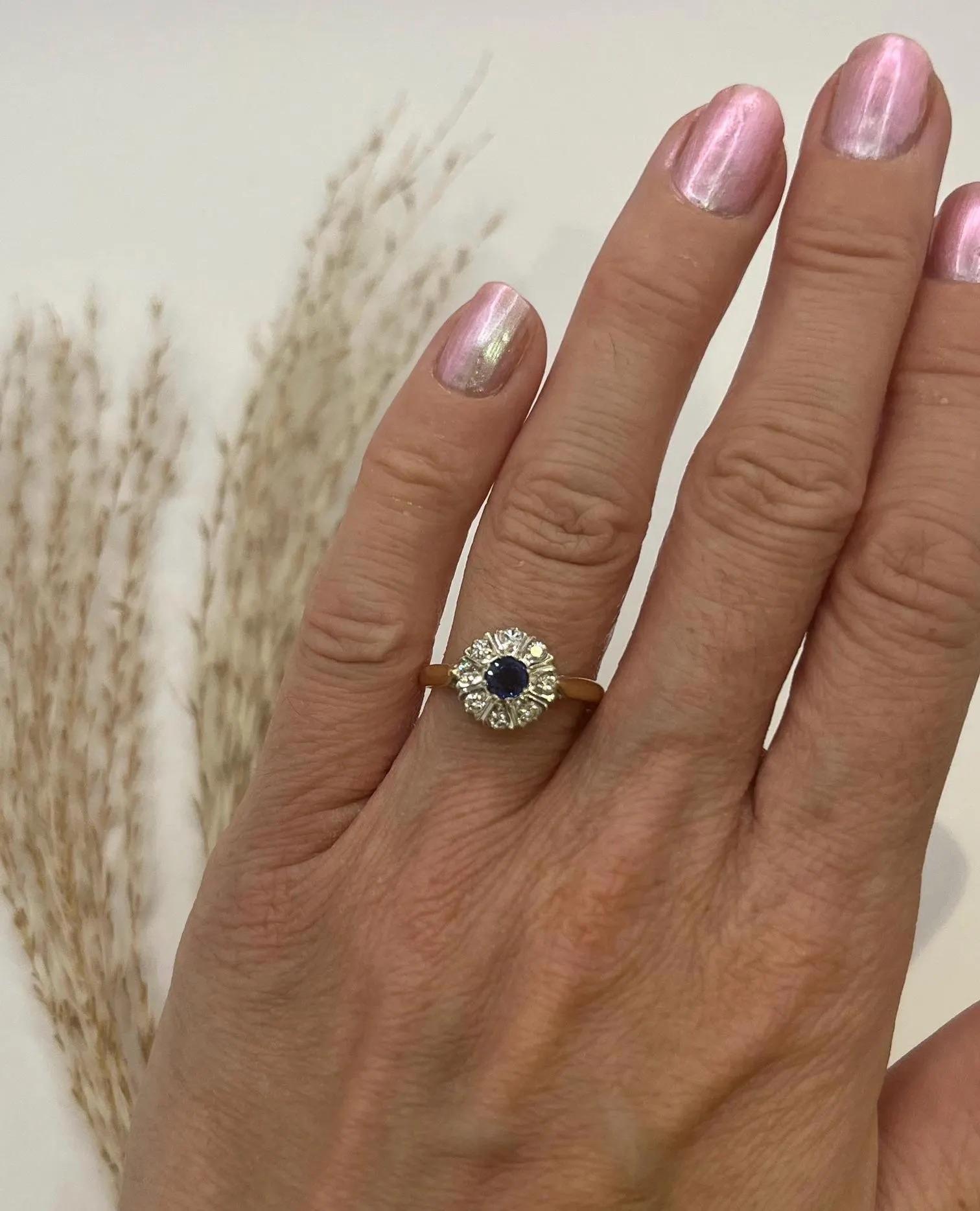 Vintage Saphir & Diamant Cluster Ring 

Gepunztes 18ct Gold 

Birmingham 1976

Vintage-Cluster-Ring mit einem zentralen Saphir im Rundschliff von ca. 0,20 ct, umgeben von acht Diamanten im Brillantschliff von insgesamt ca. 0,16 ct. 
Die Steine sind