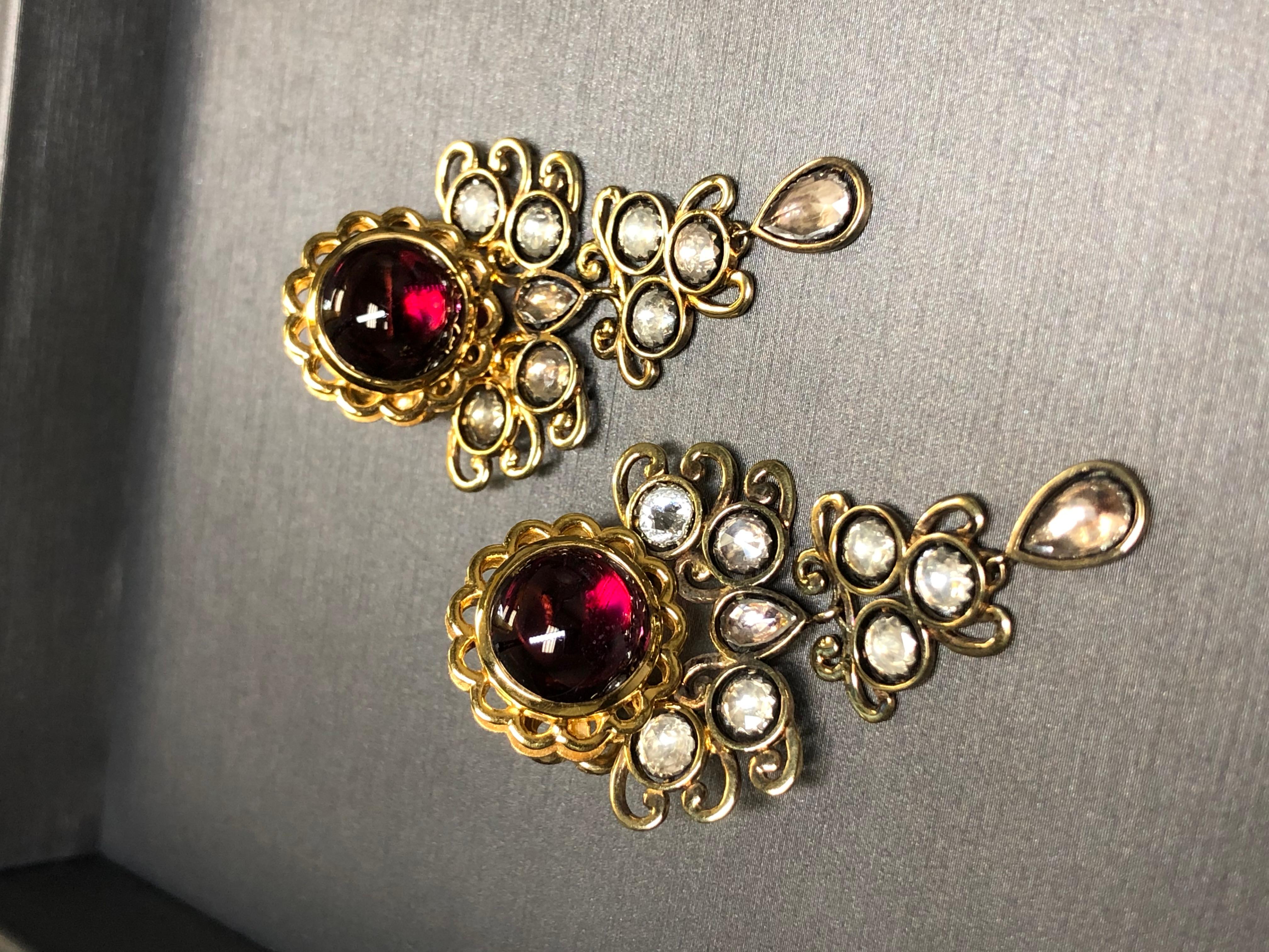 
A beautiful and ornate pair of earrings done in 18K yellow gold and centered but large cabochons of rhodolite garnet (10.4mm in diameter) atop numerous foil-backed rose cut natural quartz. A simply designed pair of earrings with such a regal look.