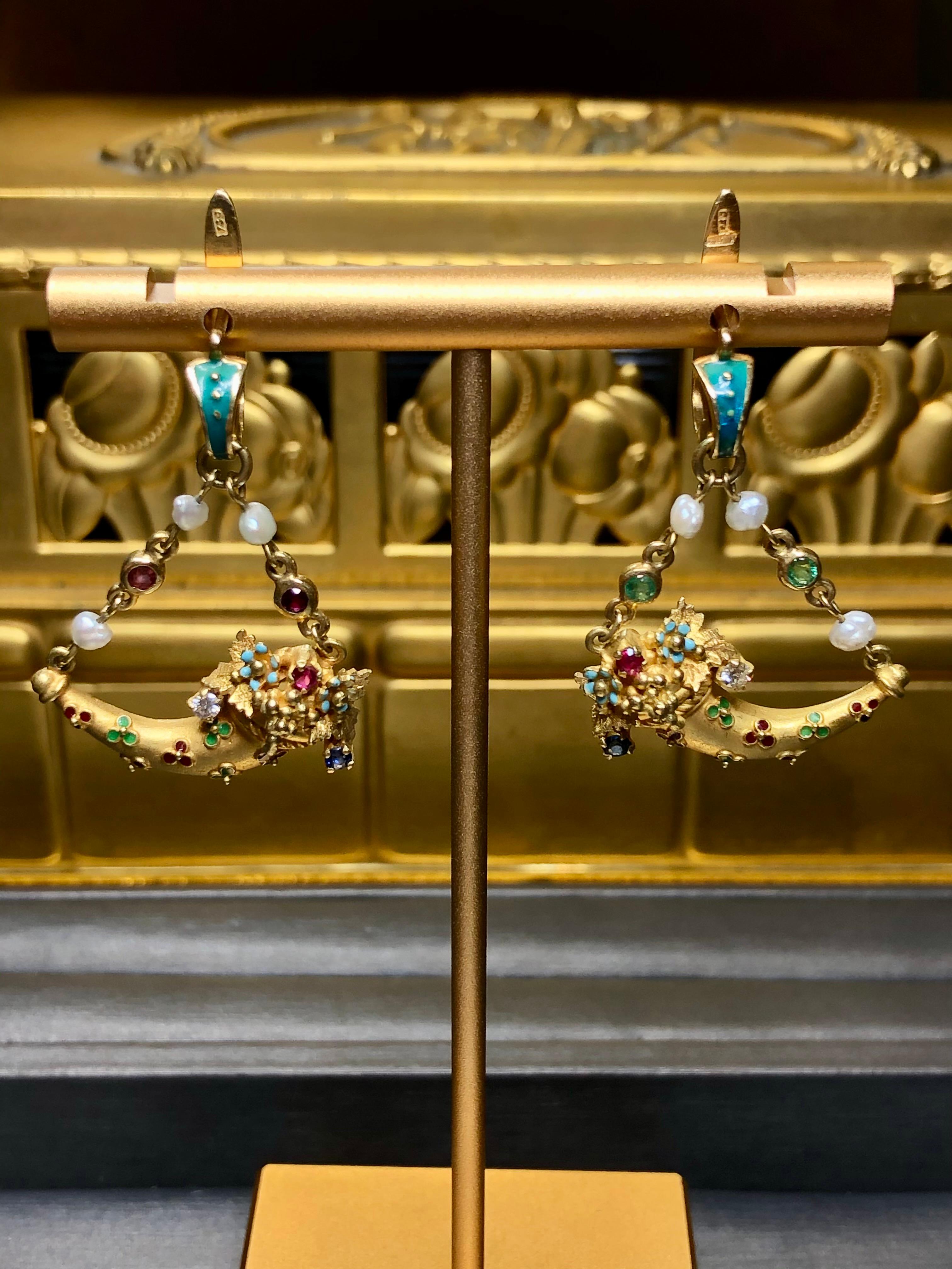 Uno stravagante paio di orecchini della metà degli anni '50 in oro giallo 18 carati a forma di cornucopie stilizzate. Sono stati rifiniti con smalto e infilati con perle e incastonati con rubini naturali, zaffiri, smeraldi e circa 0,15 carati di