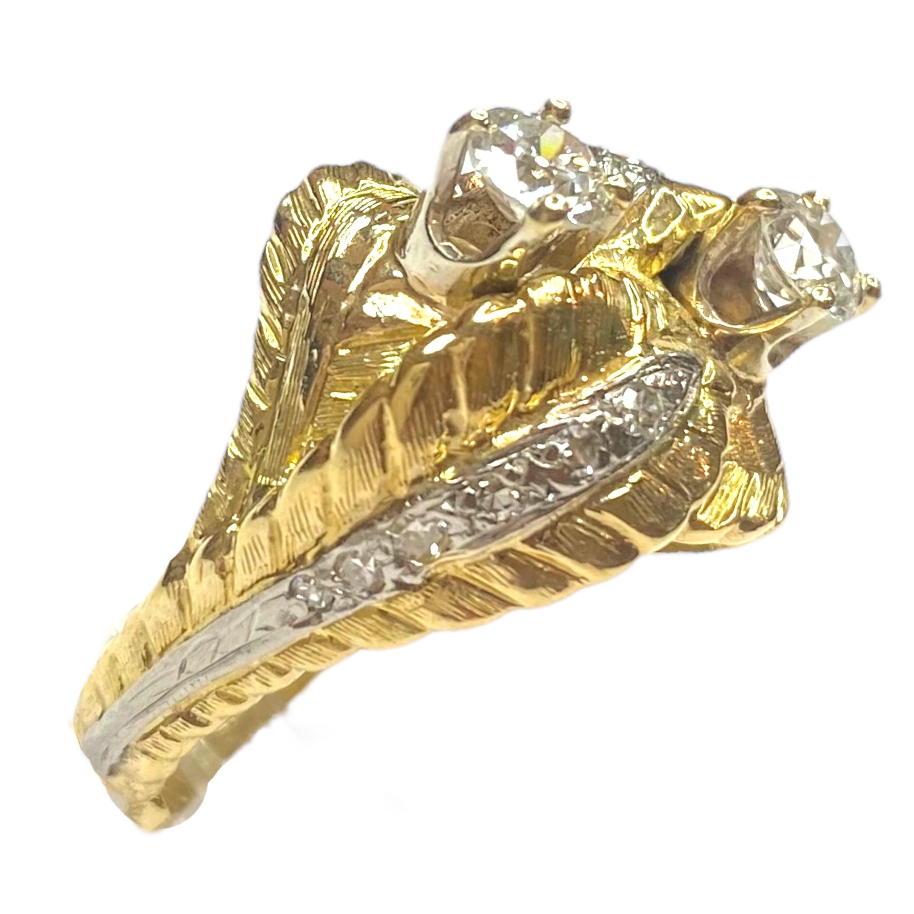 Elaborado en oro de 18 quilates, el anillo presenta un diseño cruzado abovedado de oro amarillo con dos solitarios de diamantes engastados en oro blanco en una montura de diamantes engarzados de estilo foliado. 
Acabado texturizado con detalles de