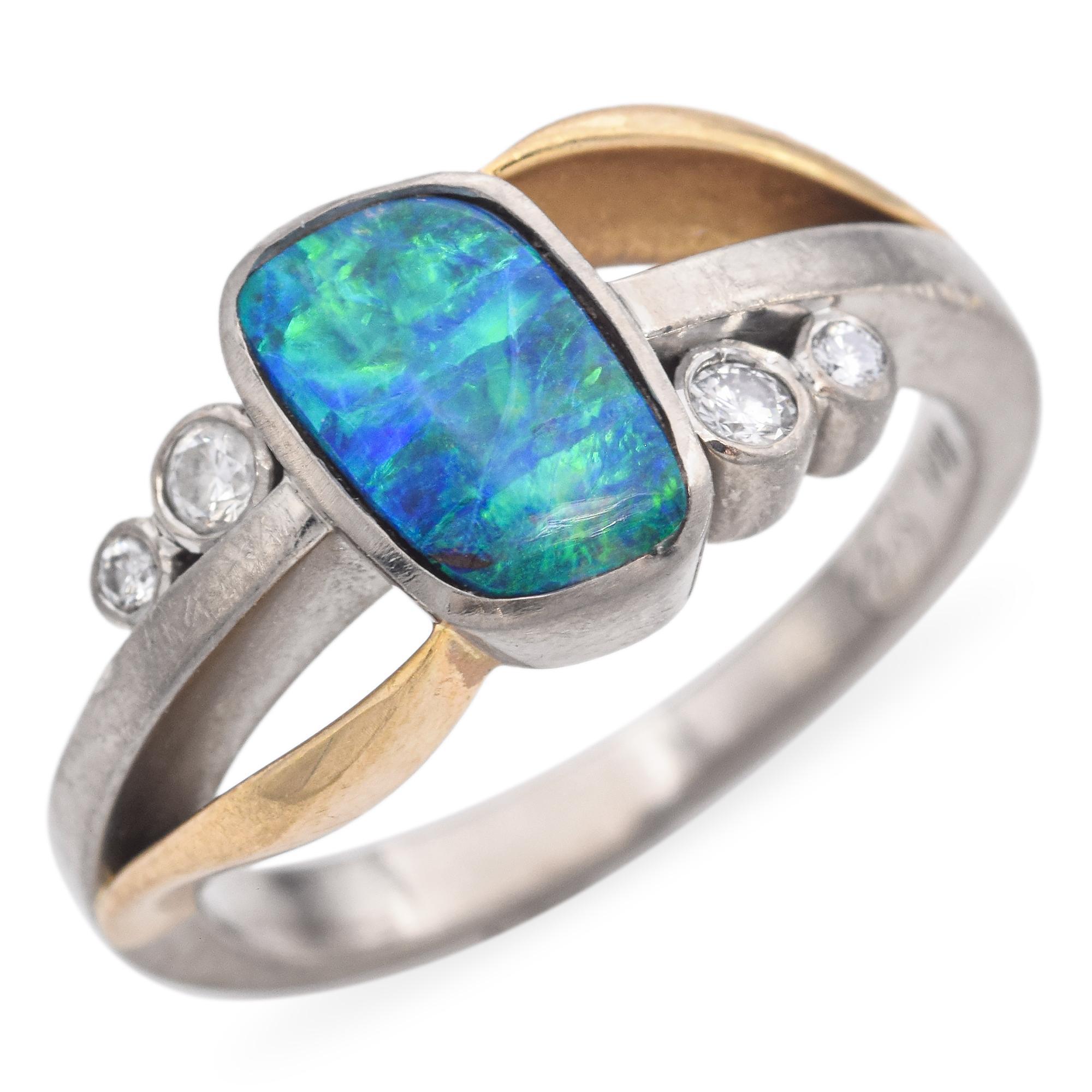 C. 20th Century This striking ring is crafted in 18k yellow and white gold. It features a captivating blue black opal, weighing approximately 0.8 carats. The opal is complemented by round white diamonds, each weighing 0.05 carats. The design