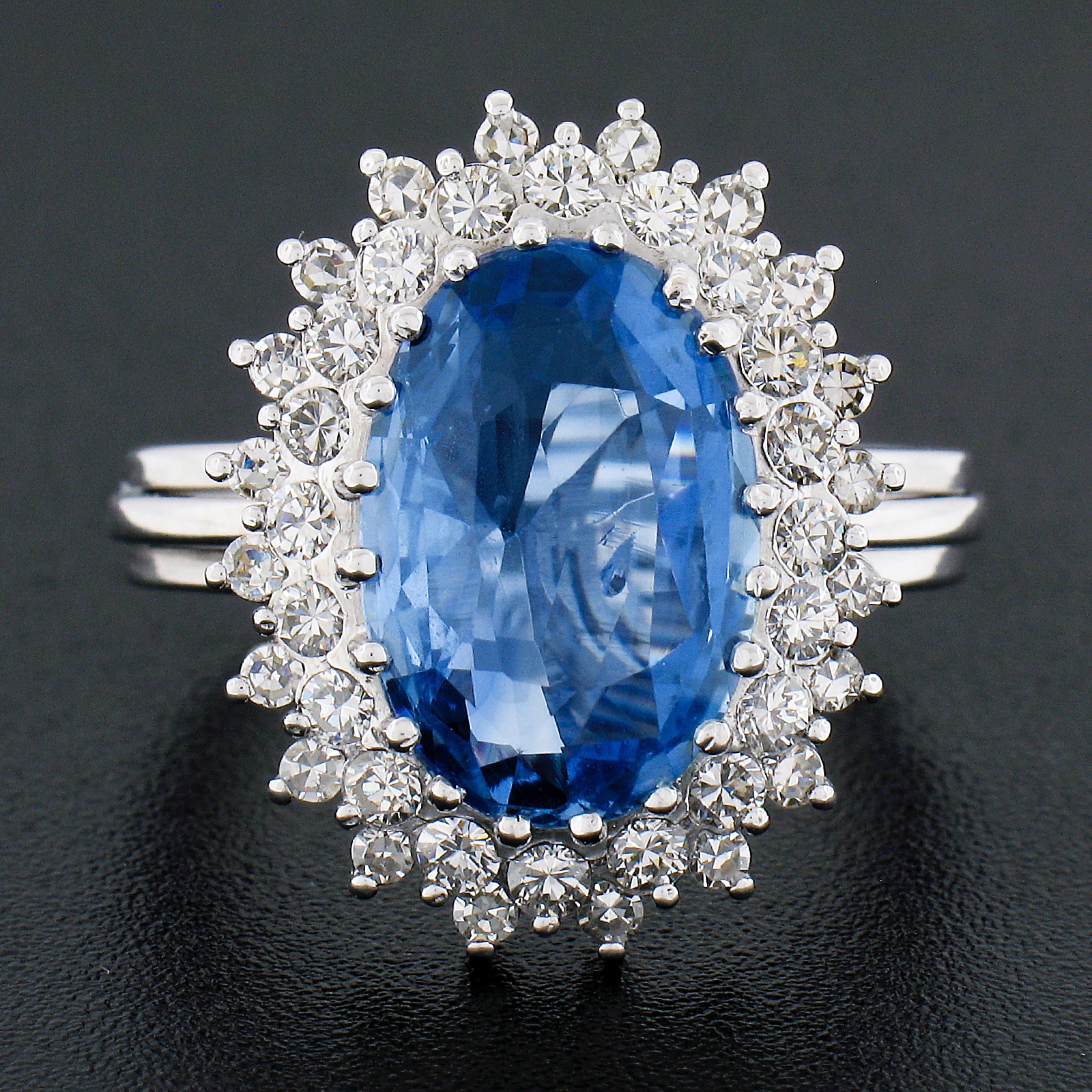 This jaw dropping vintage cocktail statement ring is crafted in solid 18k white gold and features a gorgeous, GIA certified, oval brilliant cut sapphire set at the center of a magnificent diamond dual halo. The large sapphire weighs approximately