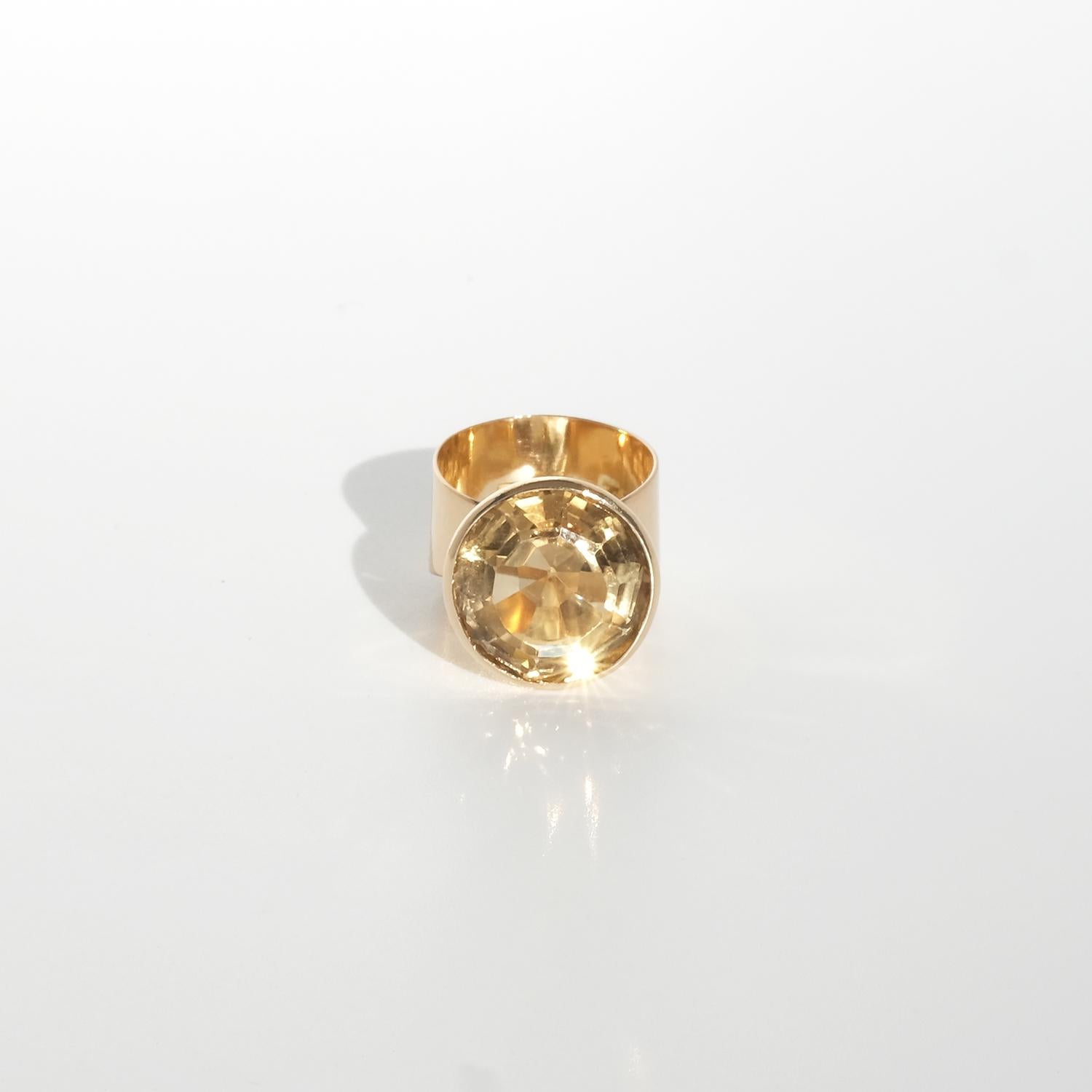 This vintage 18-karat gold ring showcases a large, round faceted citrine in a warm golden hue, radiating brilliance with every facet. The gemstone is set in a bold, conical bezel setting reminiscent of a spotlight, drawing attention to the stone's