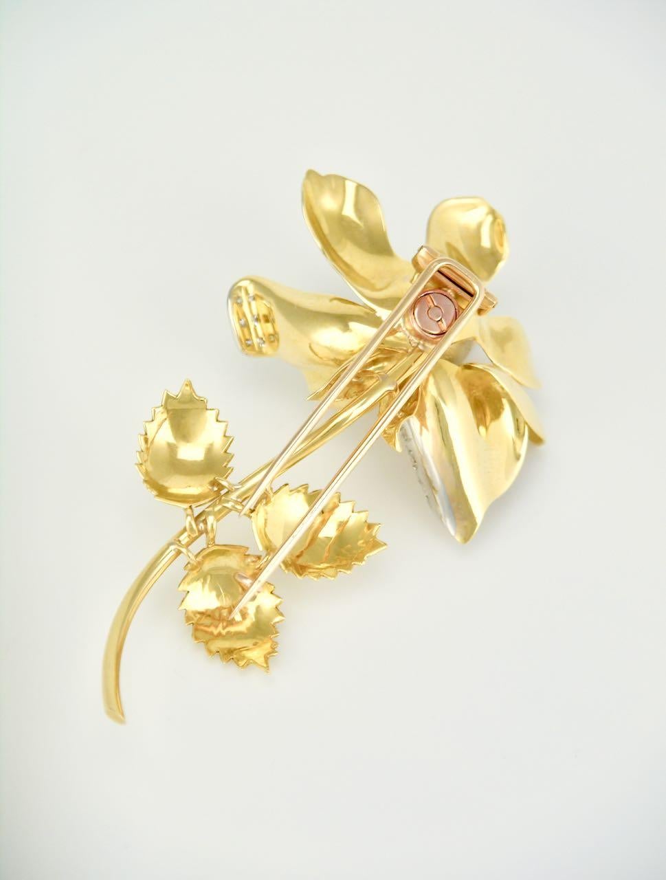 A beautifully realised pin in the form of a realistic rose shape with open petals with the tips decorated in diamonds. The yellow gold is textured with a brushed finish to the flower and leaves, and then contrasted with a polished finish to the stem