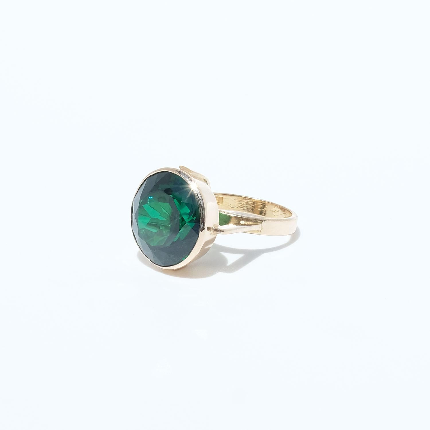 Dieser Ring aus 18 Karat Gold ist mit einem tiefgrünen synthetischen Spinell verziert. Die Fassung ist prominent und wird von zwei goldenen Schultern getragen, die aus dem Ringschaft herausragen.

Dies ist ein Cocktailring für alle Liebhaber der