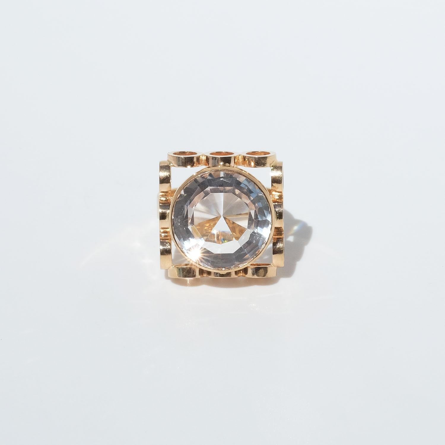 This 18 karat gold ring is adorned with a large brilliant cut rock crystal. The setting has an unusual shape being decorated with joined circles, and when looking at the ring from above these circles create a prominent square frame around the
