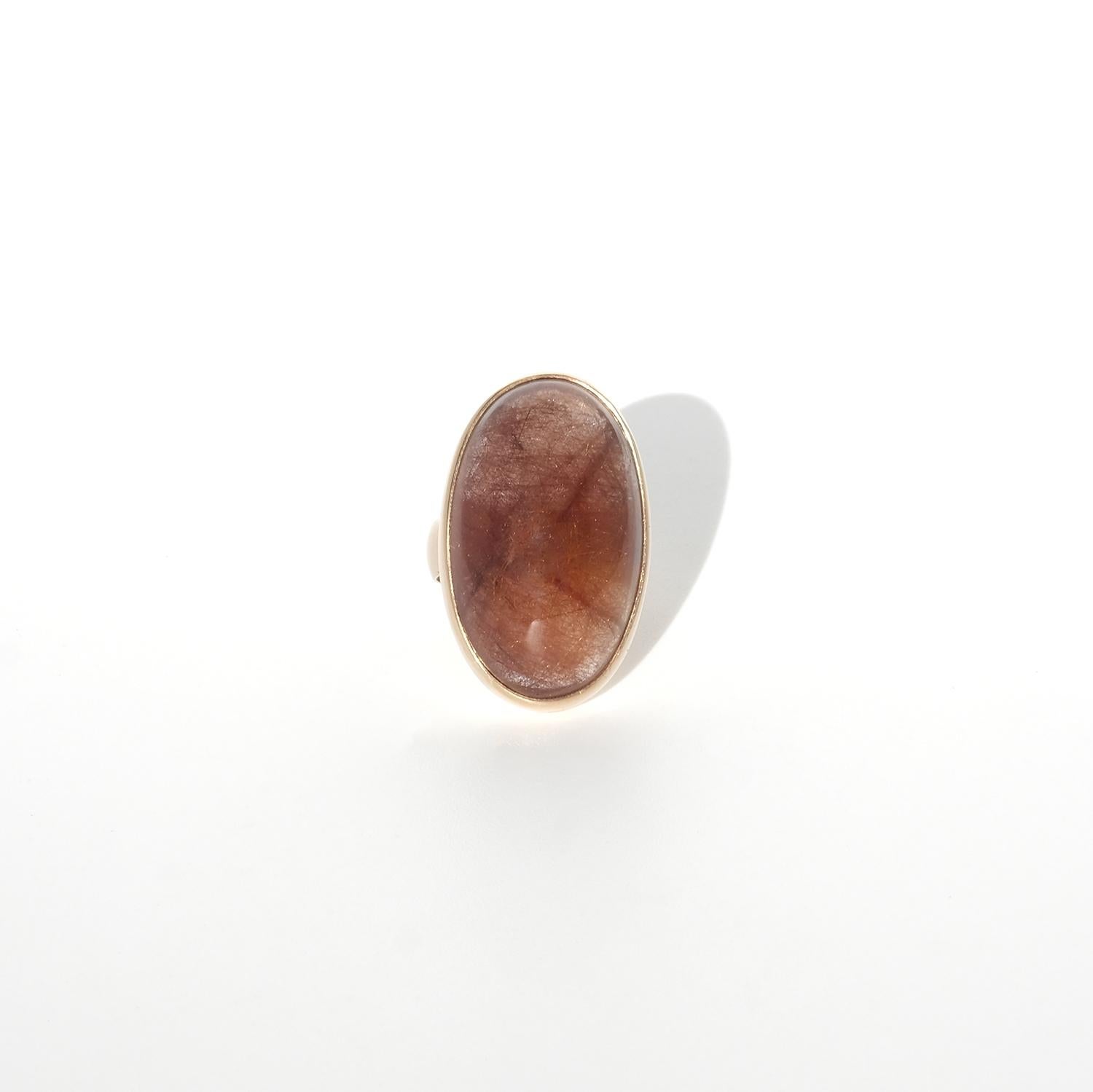 Questo anello vintage presenta un affascinante quarzo rutilo ovale tagliato a cabochon, che mostra profonde tonalità bruno-rossastre con delicate inclusioni aghiformi che aggiungono profondità e carattere. La pietra è incastonata in un castone d'oro