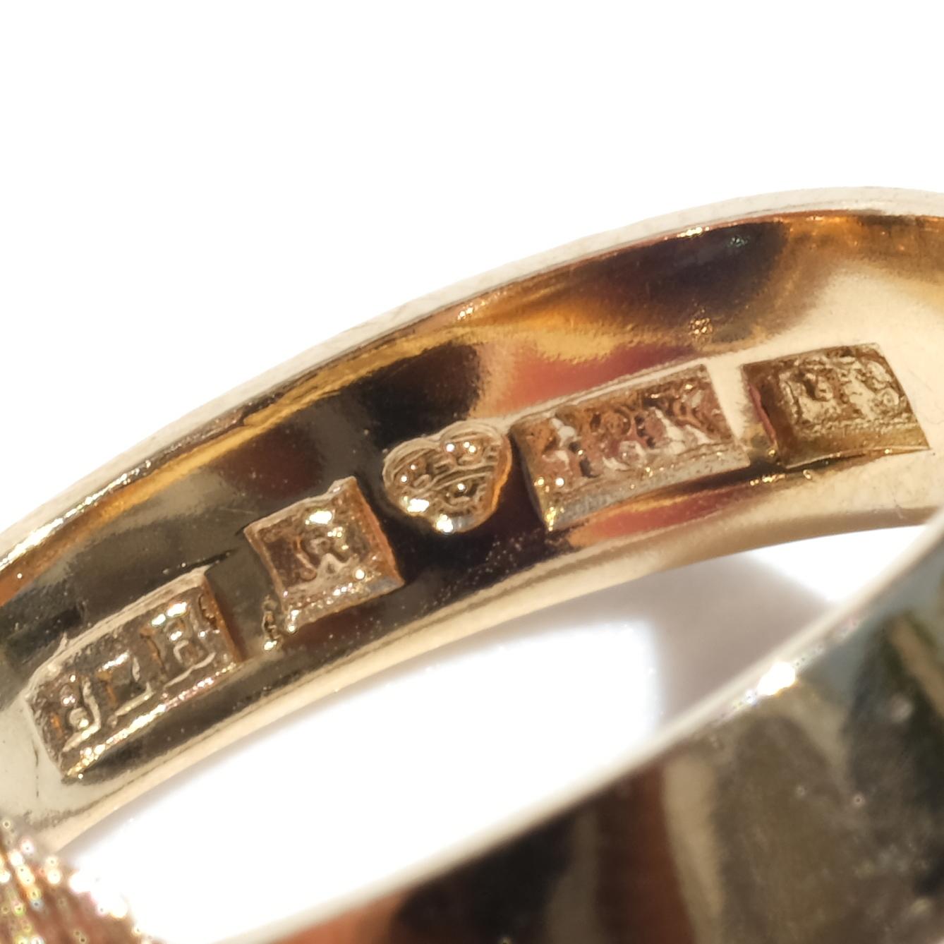 Este anillo vintage tiene una banda de oro de 18 quilates con un engaste texturizado único. El engaste está esculpido con motivos geométricos y angulosos que envuelven la espinela sintética verde. La espinela está tallada en cabujón, mostrando una