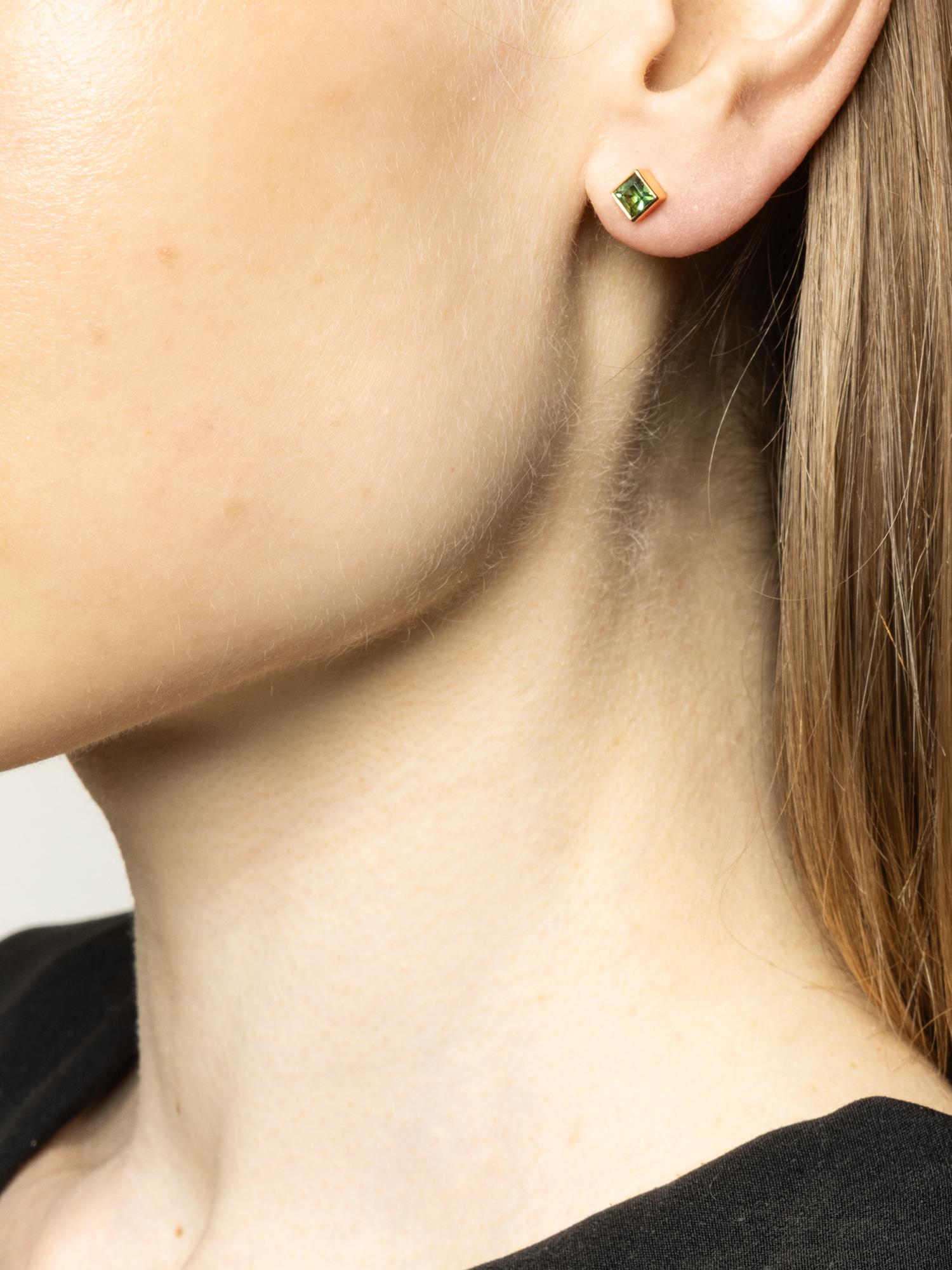 These 18-karat gold stud earrings feature square settings that elegantly frame the square-cut tourmaline gemstones. The tourmalines display a vibrant green colour, adding a touch of luxury and sophistication. On the ear, the earrings sit delicately,