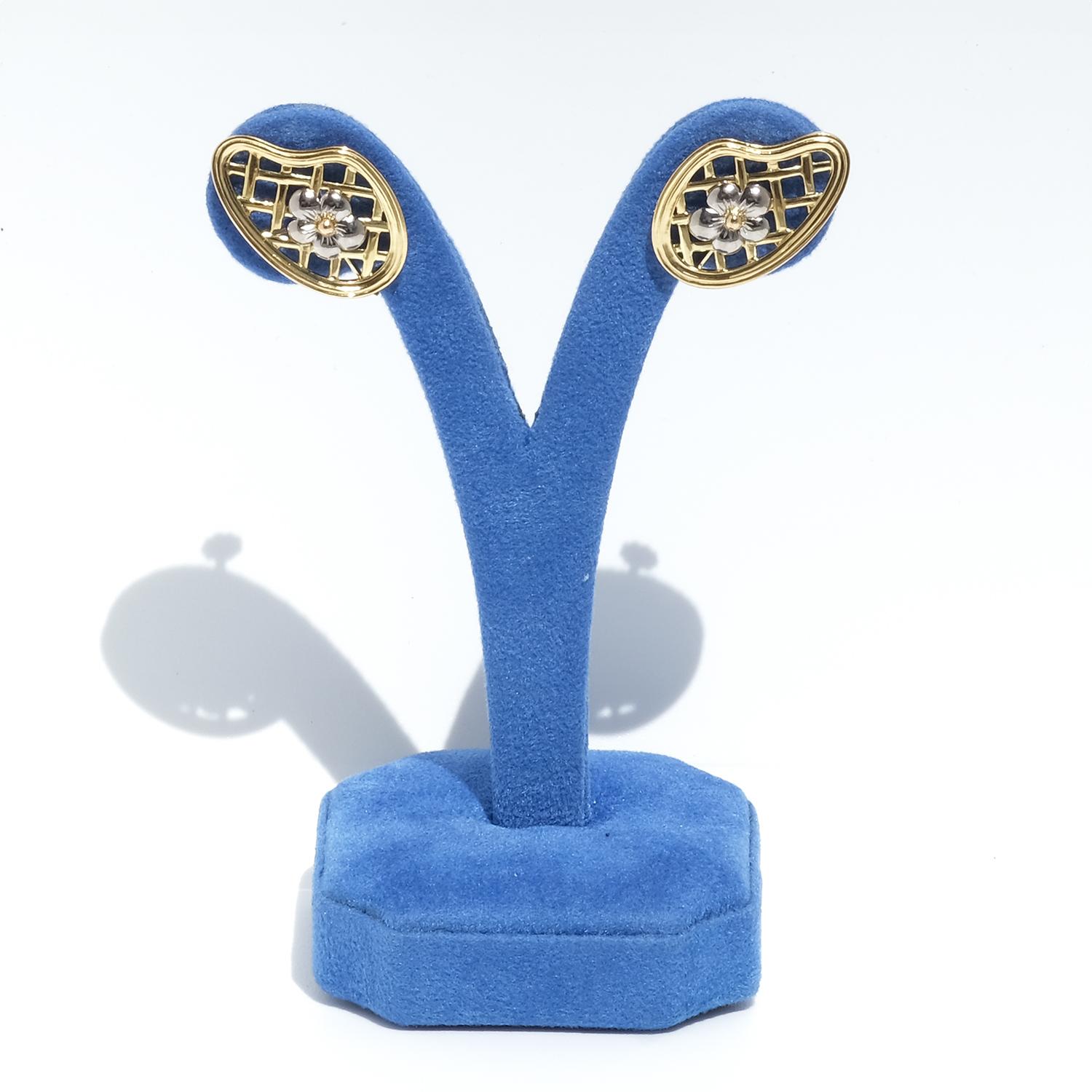 These unique earrings in 18-karat gold and white gold feature an intricate zigzag pattern. The earrings are shaped in an organic, asymmetrical design, enhancing their distinctiveness. At the center, detailed flowers with white gold petals showcase