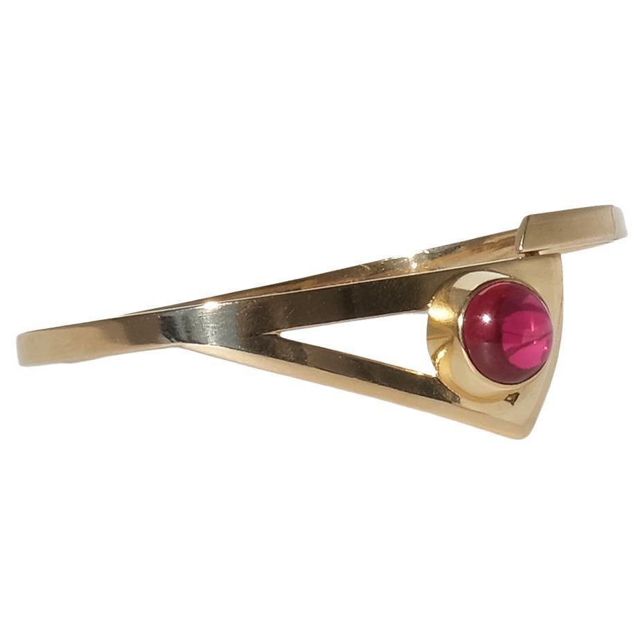 Ce bracelet vintage est réalisé en or jaune 18 carats avec une structure fixe et rigide qui s'enroule autour du poignet dans un arc épuré et minimaliste. Au sommet, elle présente une forme géométrique ouverte et asymétrique - ressemblant à un