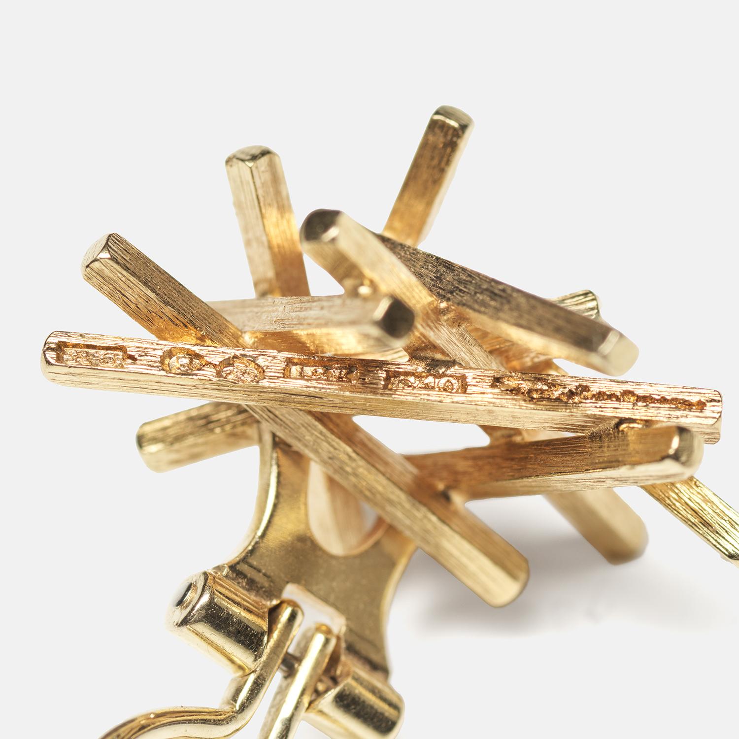 These are 18 karat gold clip earrings featuring a dynamic, abstract bundle of textured gold rods that create an intricate nest-like design. The gold has a rich, brushed finish that adds depth and a soft glow to the earrings. They secure comfortably
