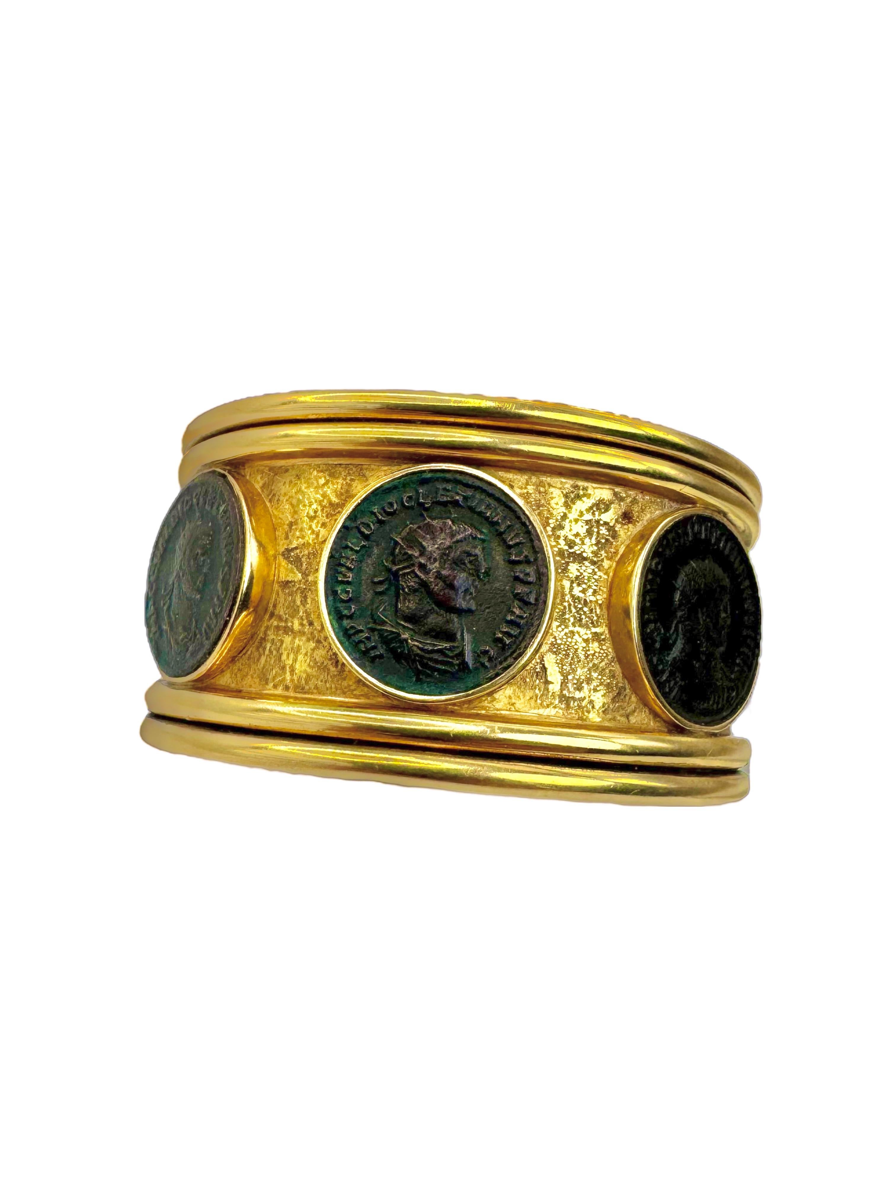 Ce remarquable bracelet manchette en or jaune 18 carats présente trois authentiques pièces de monnaie romaines en bronze, chacune étant sertie dans un chaton en relief sur un fond d'or finement martelé. La forme audacieuse et architecturale du