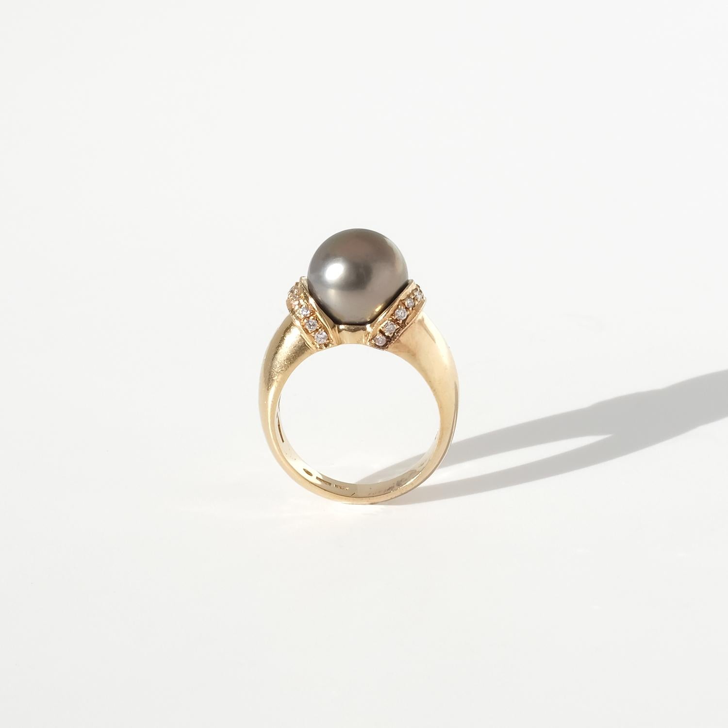 This vintage ring in 18-karat gold features a sculpted, vaulted band that gradually widens as it approaches the setting, giving the piece a balanced, architectural presence. The setting rises like a refined collar, embracing a large cultivated