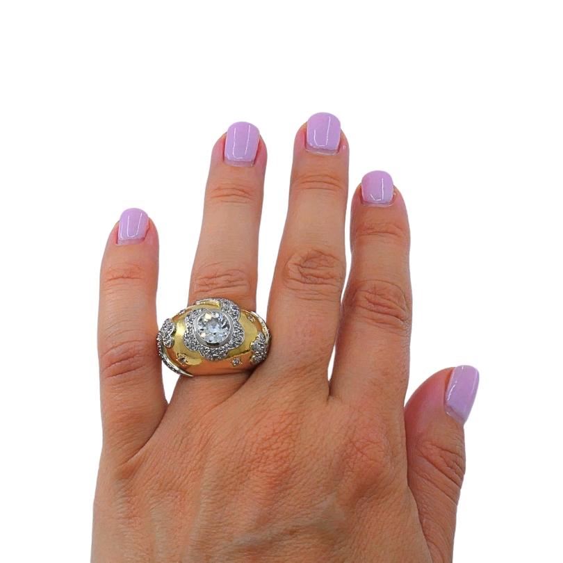 Make a bold statement with this exquisite 18K gold dome ring, featuring a floral motif. The ring is crafted in yellow gold and adorned with a central brilliant-cut diamond, beautifully framed by a halo of sparkling pavé-set diamonds in a delicate