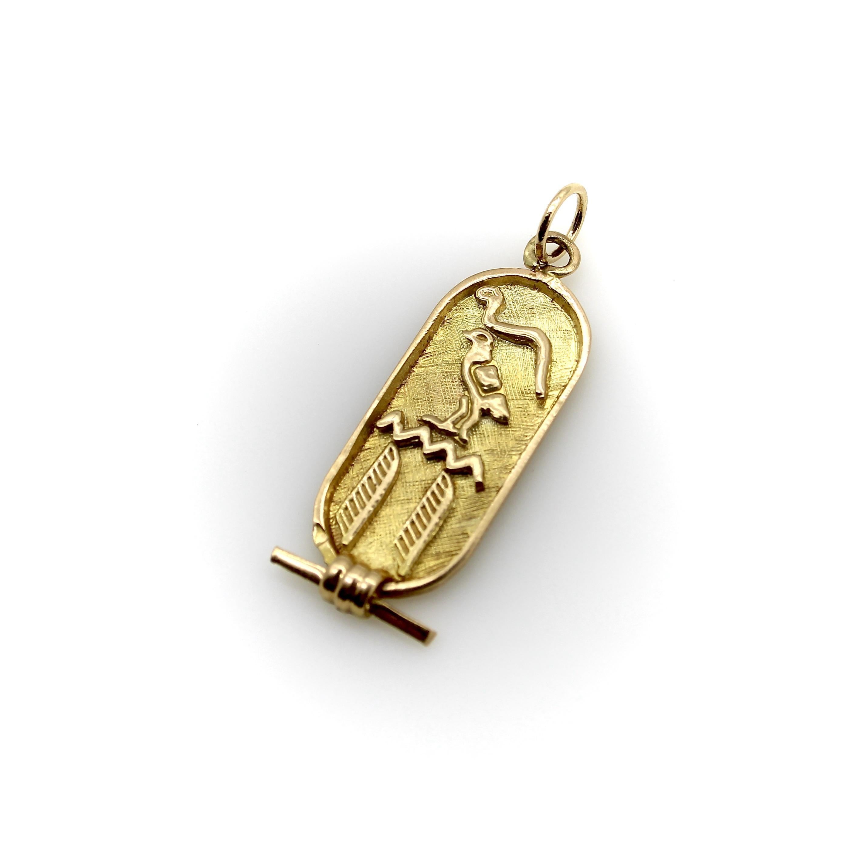 Este colgante de oro de 18 quilates se fabricó a mano en Egipto. La placa es un óvalo alargado con recortes de jeroglíficos que incluyen una serpiente, un halcón, agua y plumas. El anverso y el reverso del colgante tienen un acabado florentino