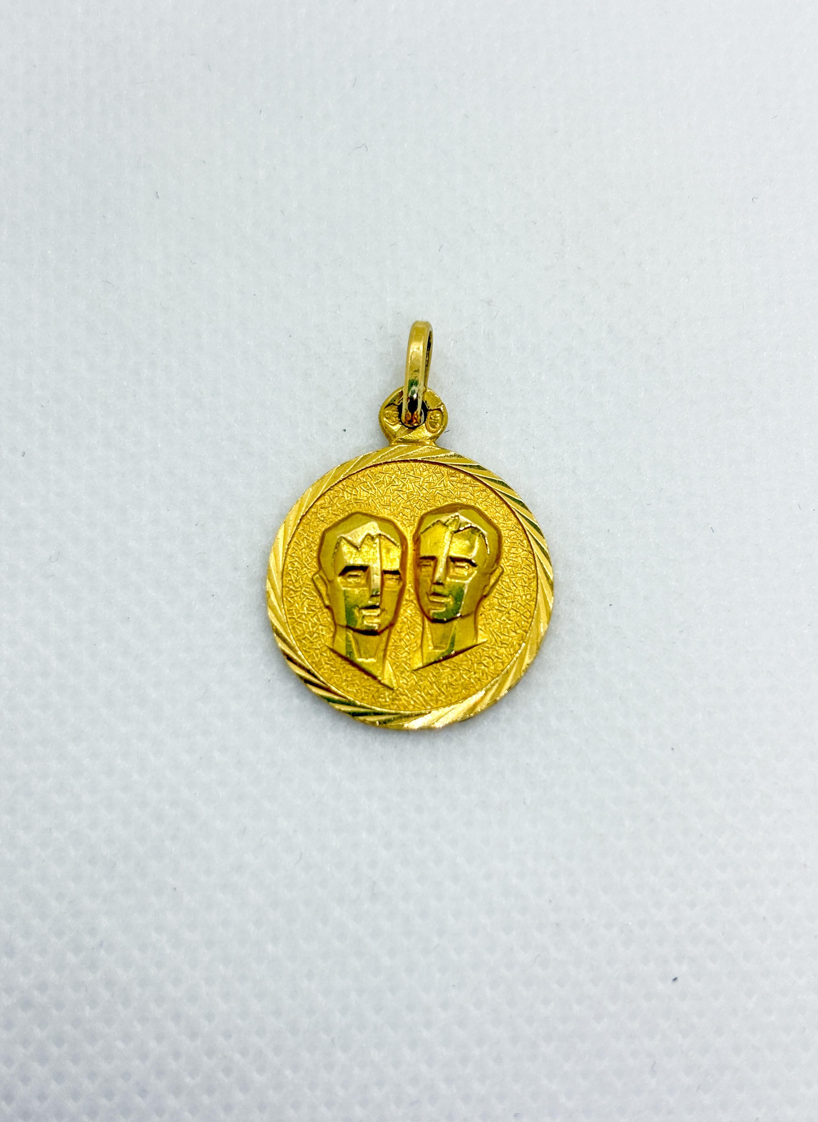 Charmanter Anhänger aus 18-karätigem Gelbgold, der das Sternzeichen der Zwillinge darstellt und in Spanien gefertigt wurde. Die Vorderseite zeigt zwei stilisierte Zwillingsprofile in erhabenem Relief, umrahmt von einer zart strukturierten und mit