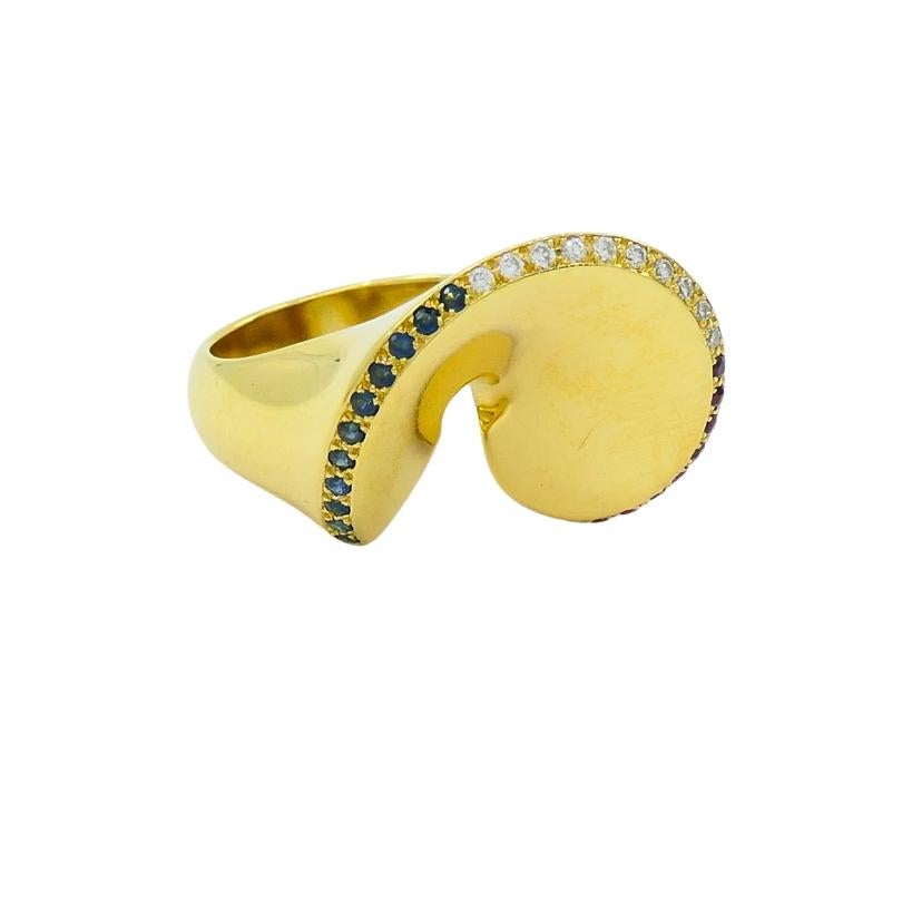 Un impressionante anello da cocktail in oro 18 carati vintage con pietre preziose.
La forma dell'anello ricorda un biscotto della fortuna, con il bordo superiore ornato da una serie di zaffiri, diamanti e rubini. Le curve fluide e il design