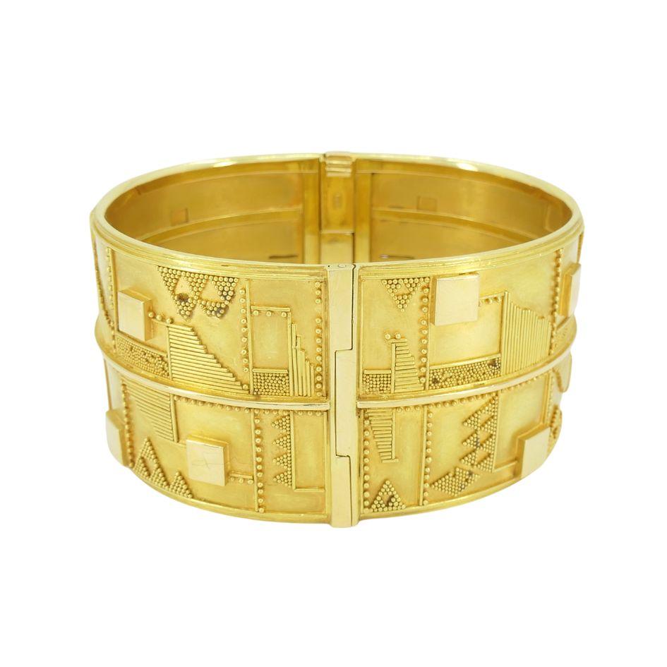 Este brazalete puño vintage de oro amarillo de 18 quilates, estampado 750 y ET, data de hacia 1930. La pieza presenta un atrevido diseño arquitectónico compuesto por motivos geométricos repetitivos, como cuadrados, triángulos y patrones lineales,
