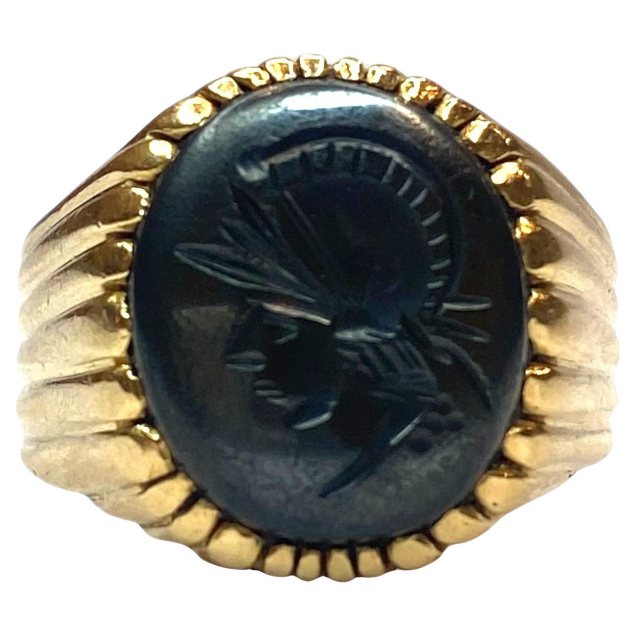 Expertly crafted in 18K yellow gold, this signet ring features a striking oval hematite stone intricately carved with a classical Roman soldier's profile. 
Wide band with a scalloped finish that complements the central design.
Measurements:
Front: