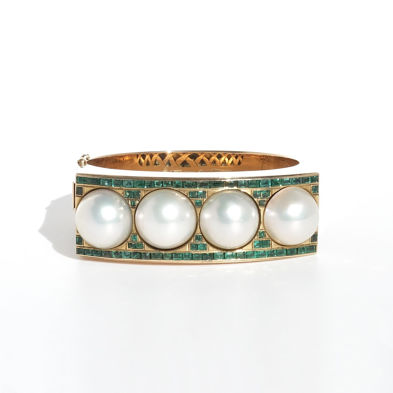 This vintage bracelet, crafted in 18-karat gold, has a substantial presence, both in weight and design. The top is adorned with four large, domed mabé pearls, their lustrous surfaces framed by vibrant green emeralds in a mix of rectangular step cuts