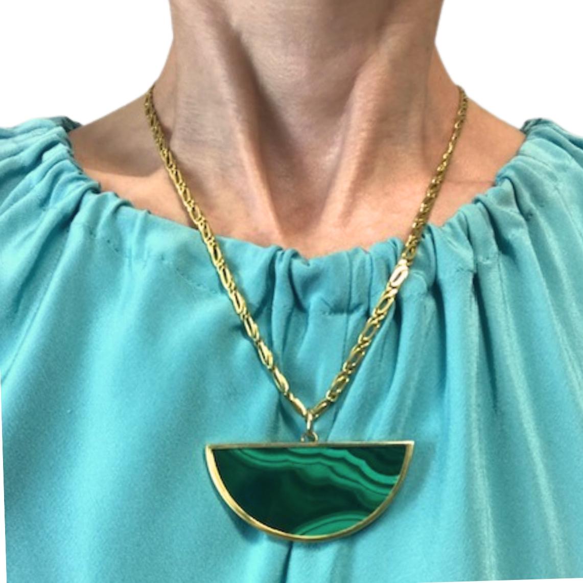 Una collana vintage in oro 18 carati con un sorprendente ciondolo di malachite abbinato a una dettagliata catena a maglie ovali. Il ciondolo ha una forma a mezzaluna, incorniciata in oro giallo 18 carati lucido. La pietra presenta splendide