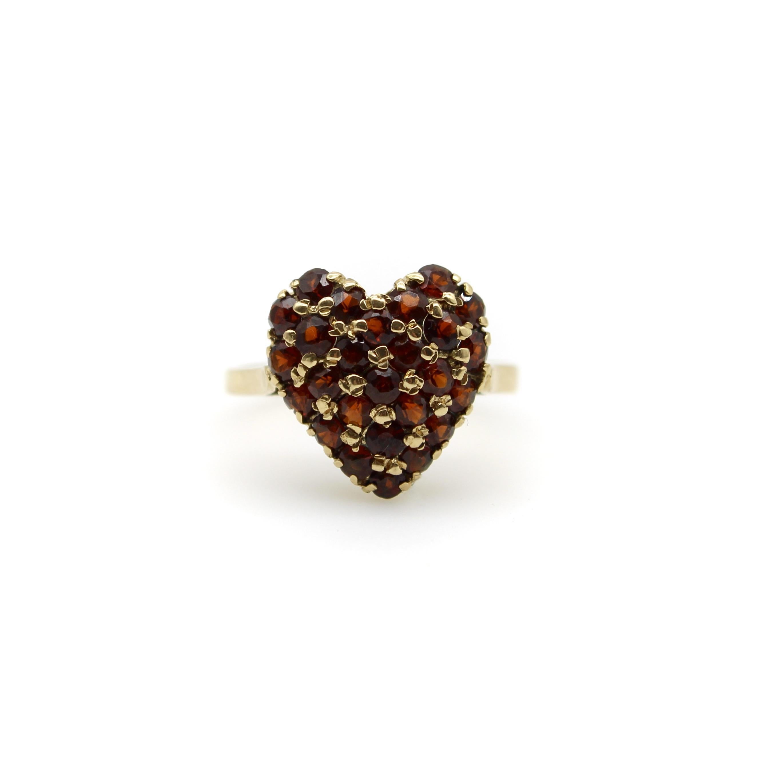 This 18k gold pave garnet ring is encrusted with 2 mm round garnets to create a beautiful sparkle of gold and wine-colored stones in a heart shape. The garnets are held in a shared bead setting, which creates an alternating pattern of gold and