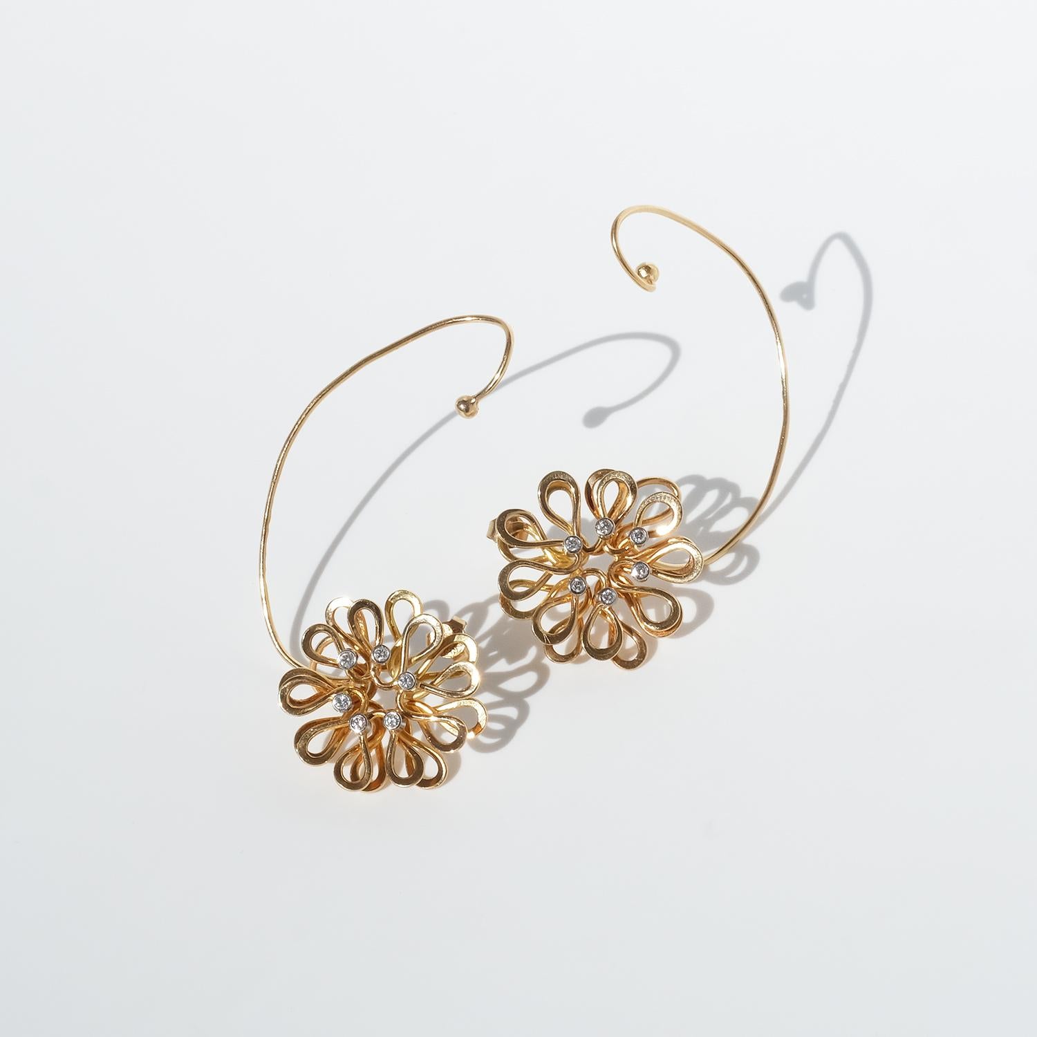 These vintage 18-karat gold earrings are designed as delicate flowers, with gold loops forming the petals. At the center of each floral element, six diamonds add sparkle and dimension. Suspended below, a slender gold bar holds a single cultured