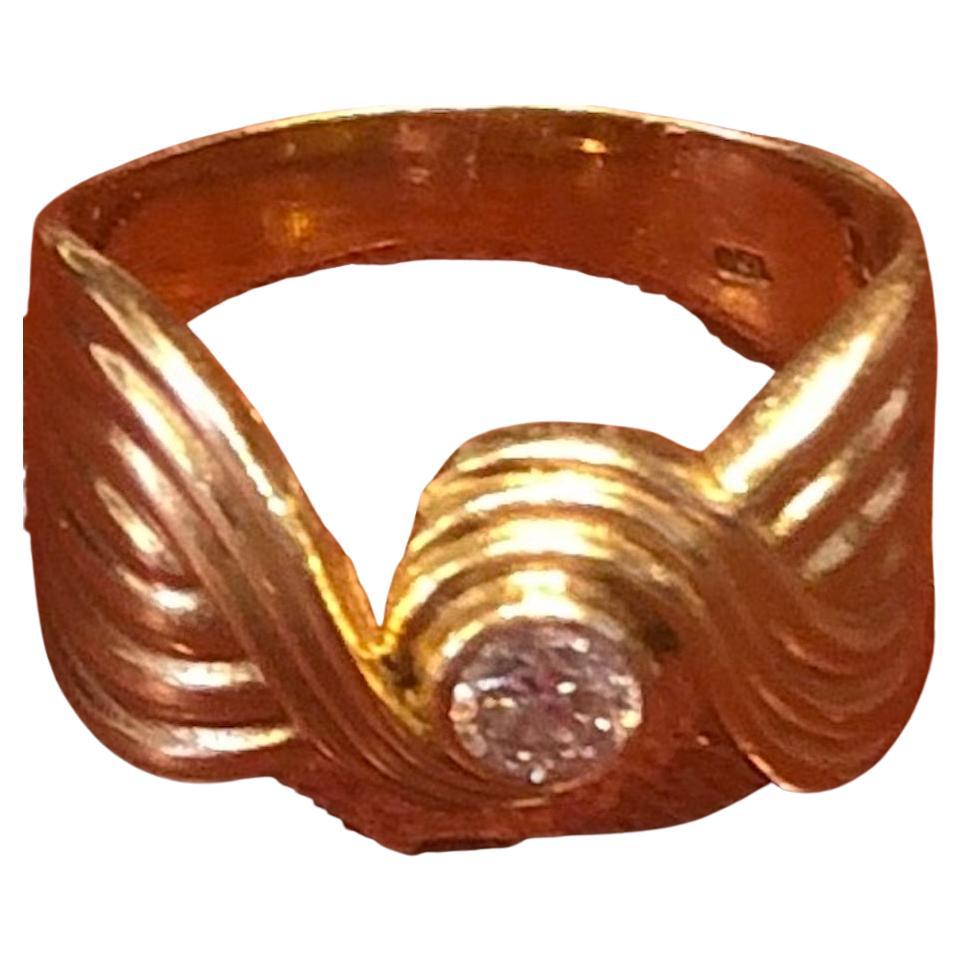 A lovely impressive vintage ring  of yellow gold with a reeded band that swirls around a round solitaire diamond weighing approximately 1/4 carat in the center of the knot.  It is marked 