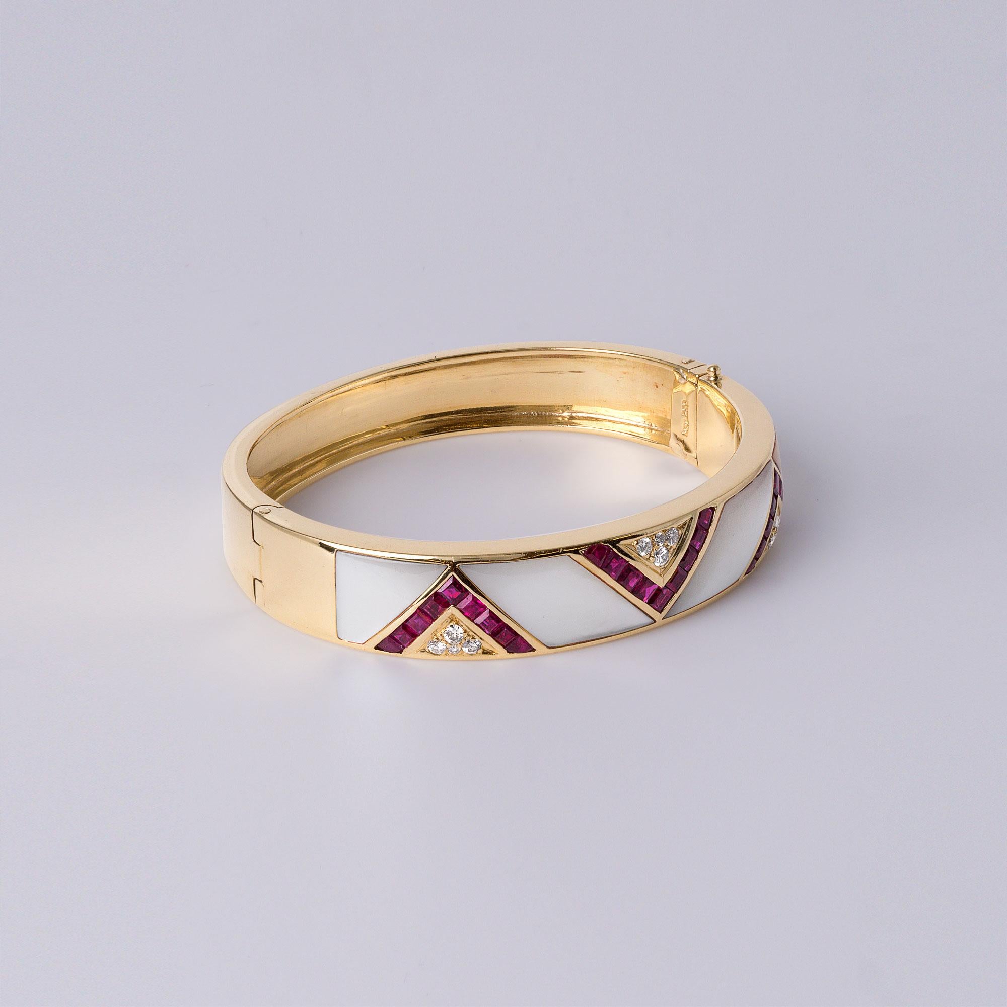 Este exquisito brazalete vintage ofrece un cautivador juego de contrastes: rubíes ardientes, nácar luminoso y diamantes centelleantes, todo ello engastado en un atrevido diseño de oro amarillo de 18 quilates. Esta pulsera irradia sofisticación y