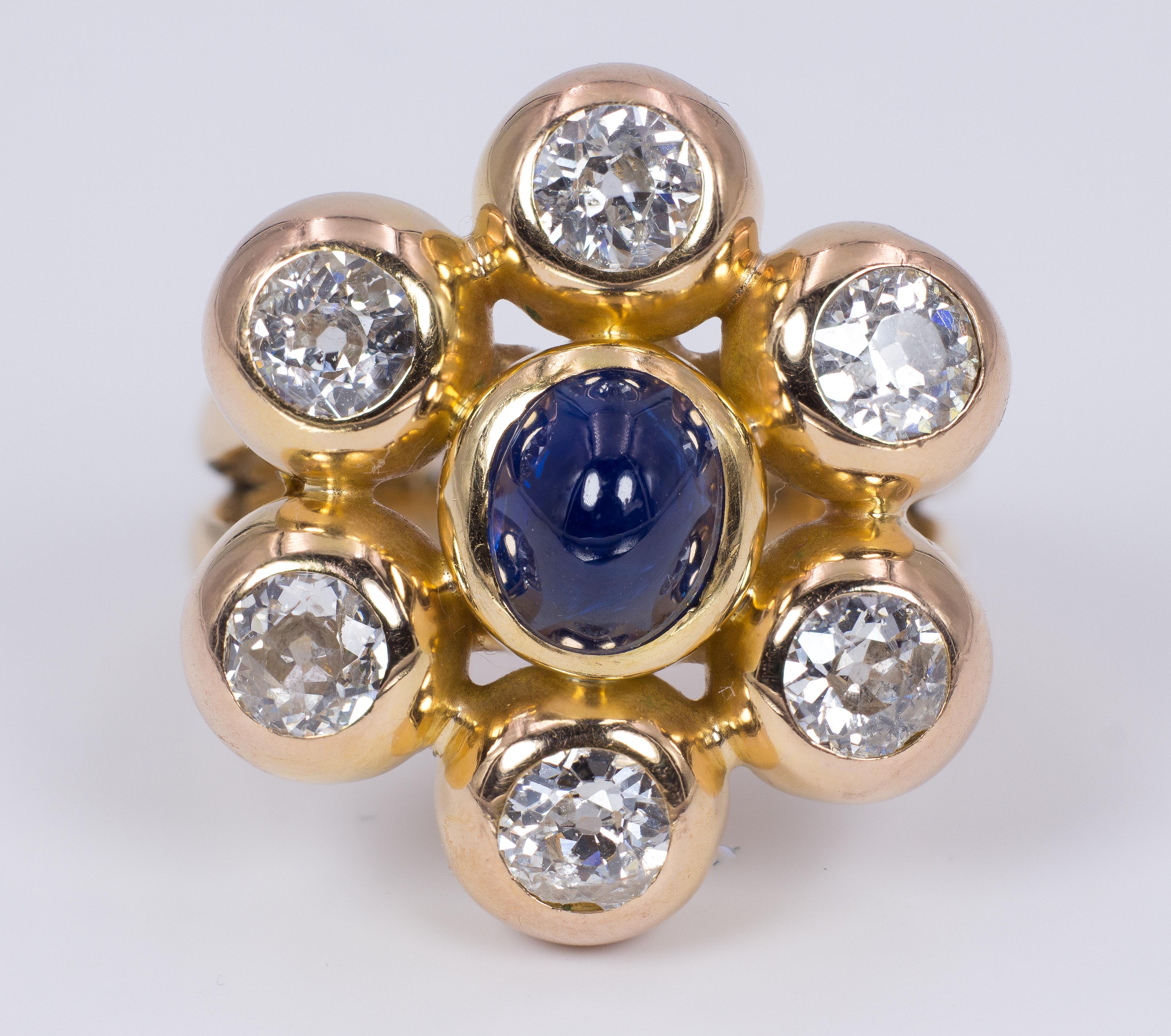 A vintage cluster ring, dating from the 1980s, with the shape of a big and colorful flower. It features a central blue cabochon sapphire, surrounded by six old European cut diamonds, for a total of more 3ct, each one set into a petal-like gold