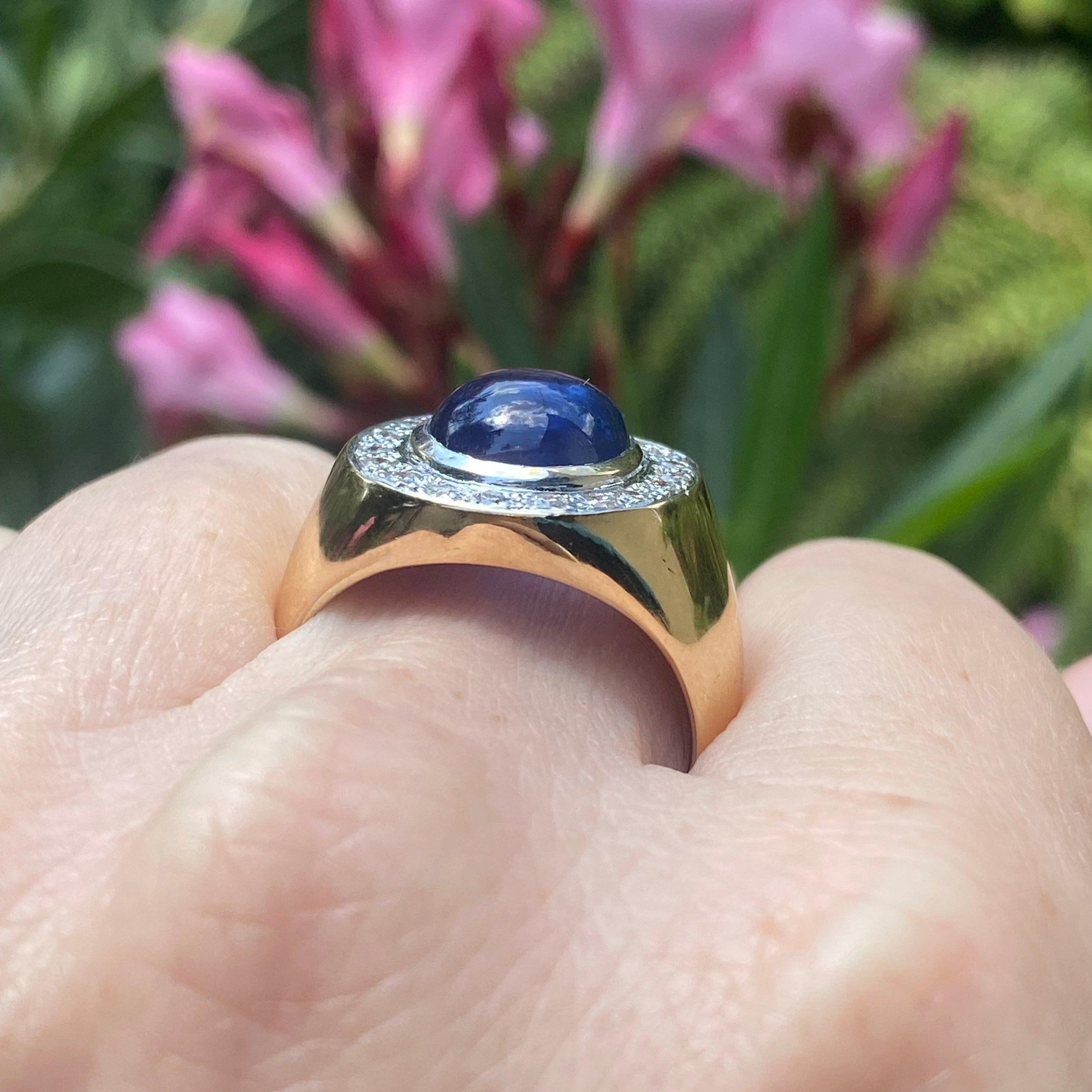 Vintage 18K gold ring featuring a round sapphire cabochon set within a bezel of diamonds, supported by fifteen millimeter wide shoulders tapering down to a five and a half millimeter wide band. Bright polish finish.
Sapphire: approx. 4 carats
19