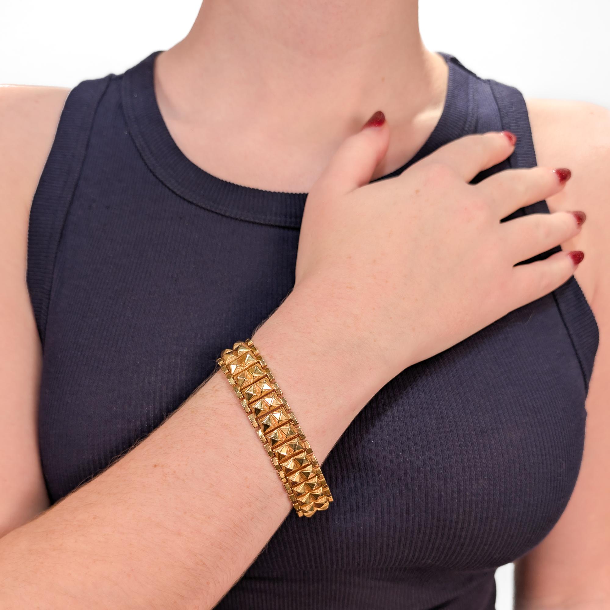 Un raffinato braccialetto stile carrarmato di proprietà.

In oro 18 carati (con una leggera sfumatura rosa).

Composto da maglie d'oro a forma di doppia borchia collegate su ogni lato con una fila di maglie rettangolari strette e a punta. 

È dotato