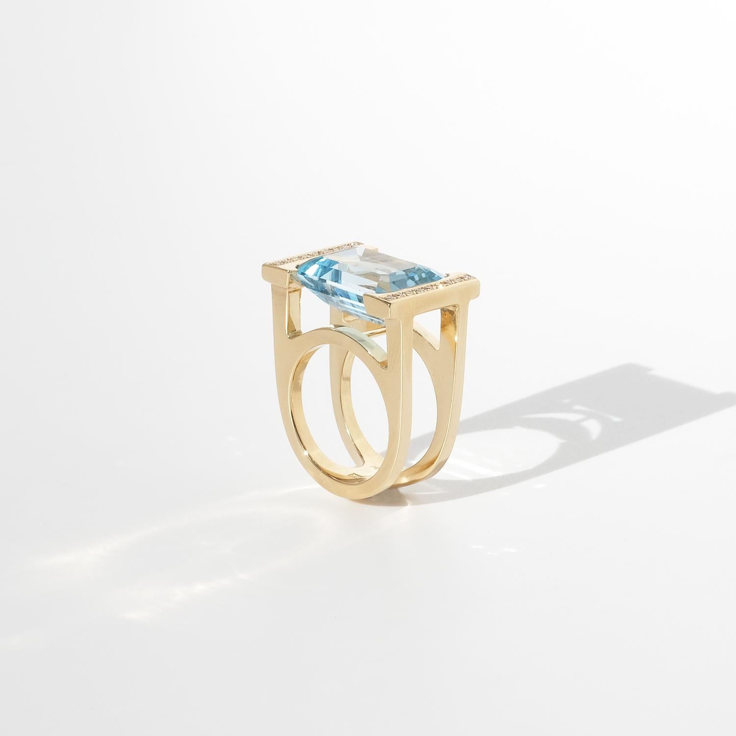 This striking vintage ring in 18-karat gold features a mesmerizing approximately 16 ct emerald-cut topaz with a vivid, radiant blue hue. The centerpiece is surrounded by 18 brilliant-cut diamonds totaling approximately 0.18 ctv, adding an exquisite