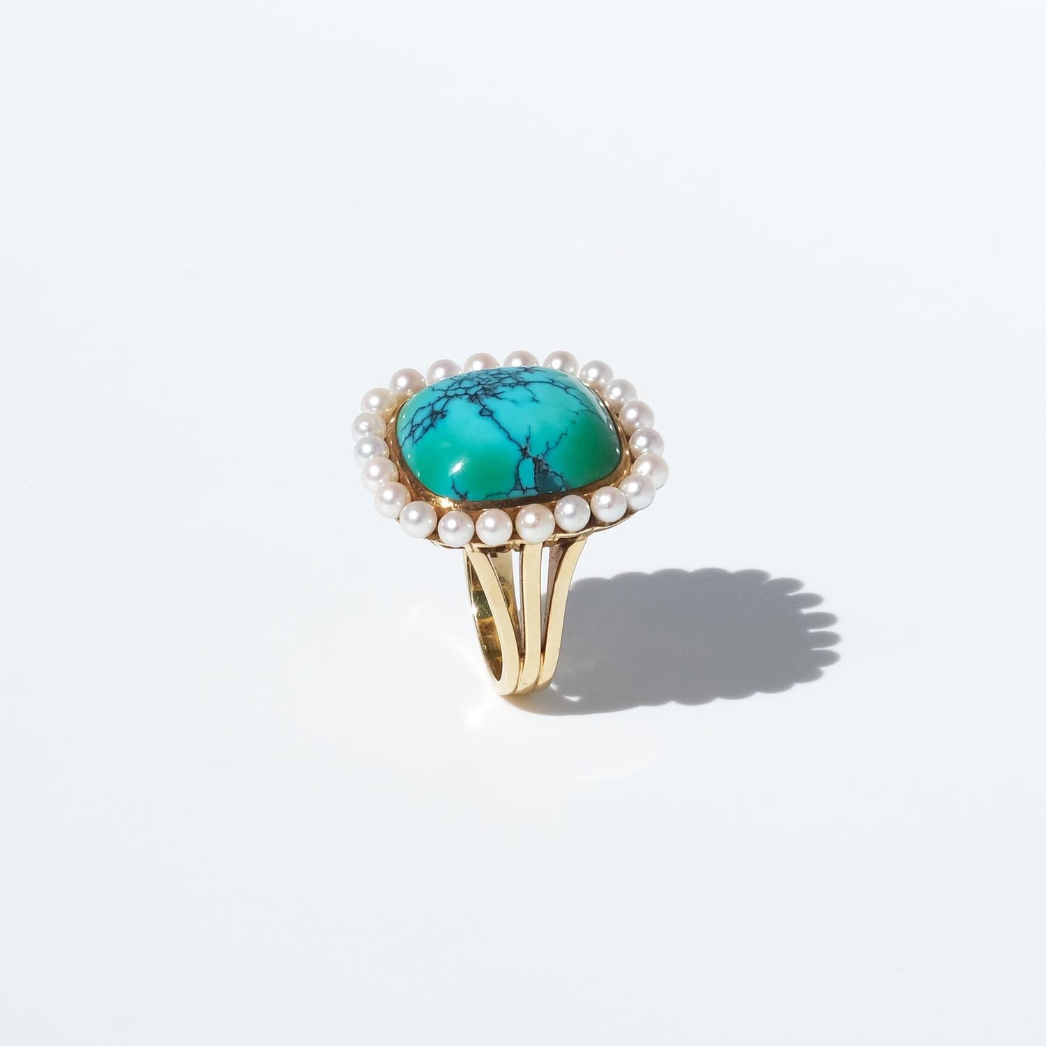 This vintage ring is crafted in 18-karat gold, featuring a nearly square adornment. At its center sits a prominent cabochon-cut turquoise with a smooth, polished surface. Surrounding the turquoise, 22 cultured pearls are meticulously set, forming an