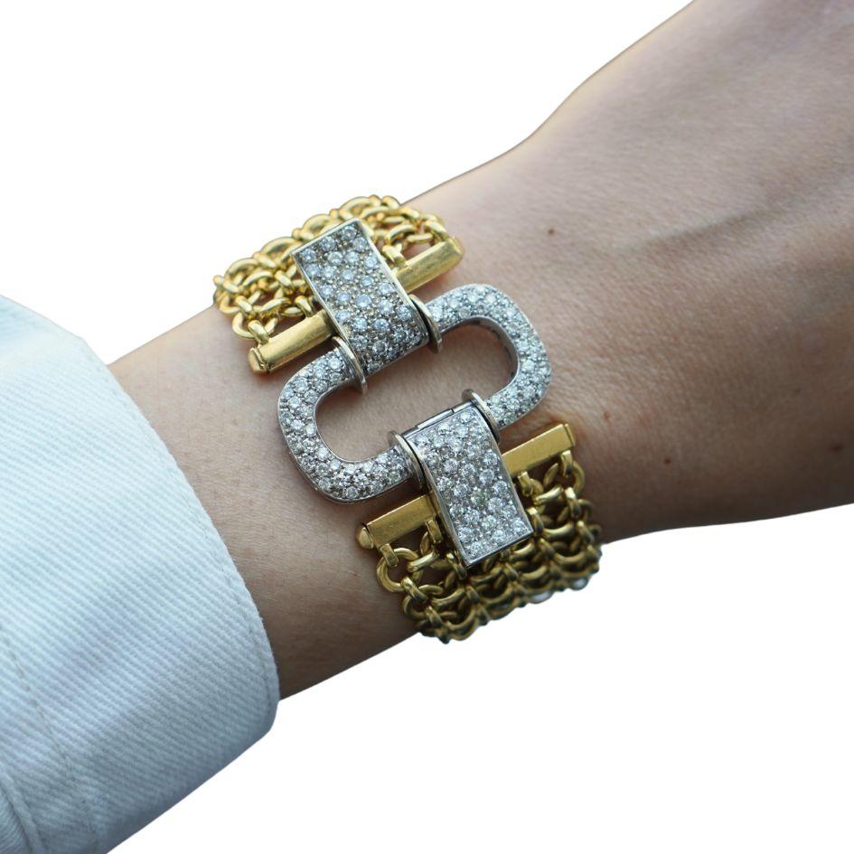 This circa 1990s 18k white and yellow gold bracelet features an elegant contrast of textures and materials. The bracelet measures 8 inches in length and has a width of 1.5 inches at its widest point. The centerpiece clasp is crafted in 18k white