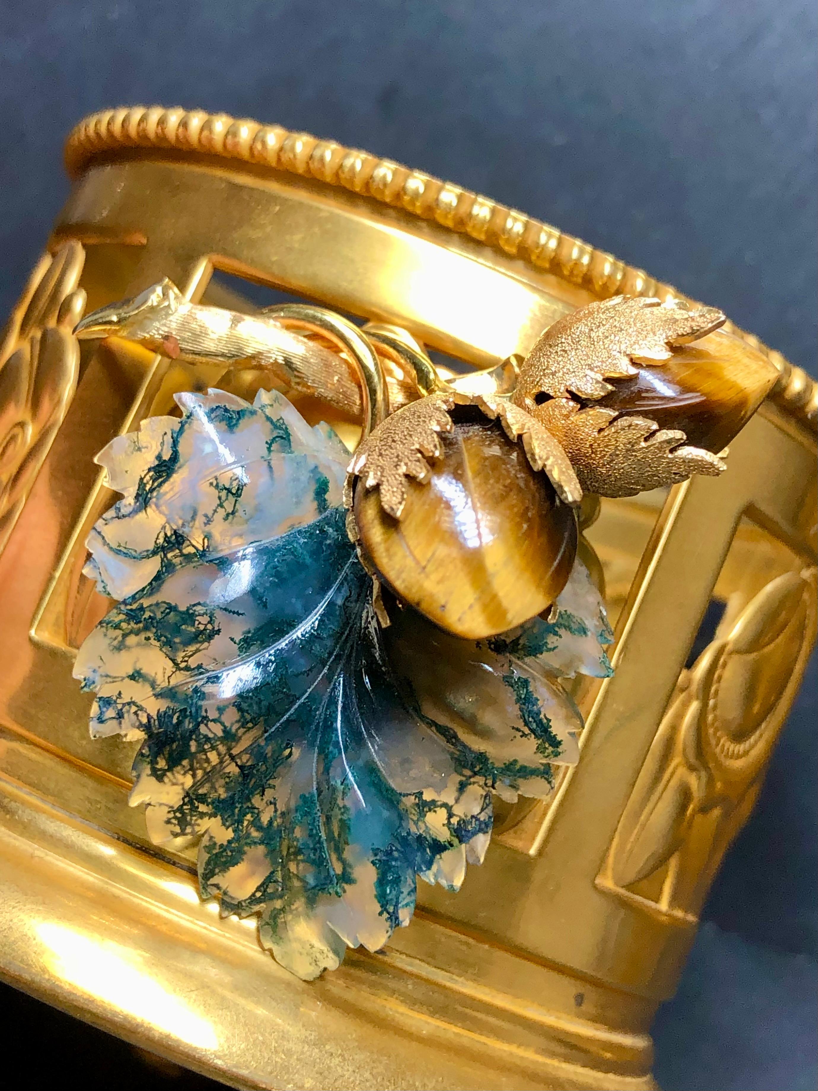 
Precioso broche hecho a mano en oro amarillo de 18 quilates (firmas y sellos pero desconocemos el fabricante) realizado como una estilizada rama de avellano. La hoja es de ágata musgosa bellamente tallada y las nueces son de ojo de tigre.