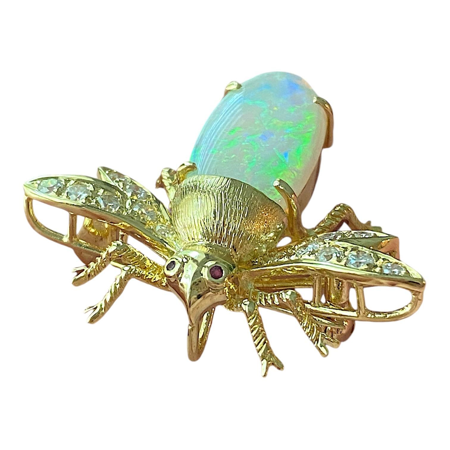 Crafted in 18K yellow gold, the pin/pendant features and insect with opal body, ruby eyes and diamond set wings. 
Opal cabochon: 2.80ct
14 round brilliant cut diamonds: 0.40ctw. Color: H-I, Clarity: SI1-SI2
Measurements: 29 mm L x 36 mm W x 11 mm H 