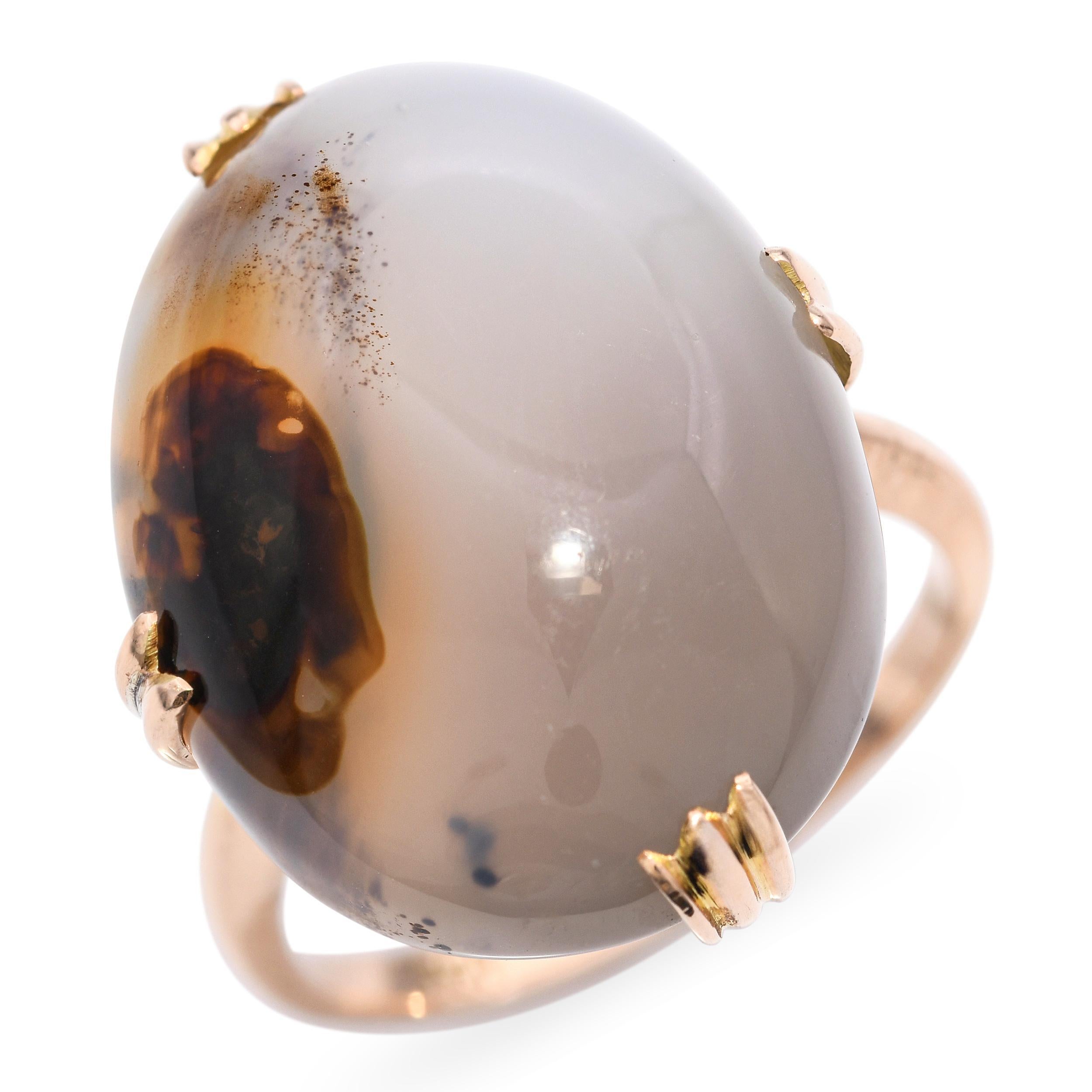 Cette bague, élégante pièce ancienne, présente une agate aux teintes riches sertie dans de l'or rose 18 carats. La pierre lisse et polie est encadrée par un chaton minimal mais classique, permettant à la bande naturelle et aux tons terreux de