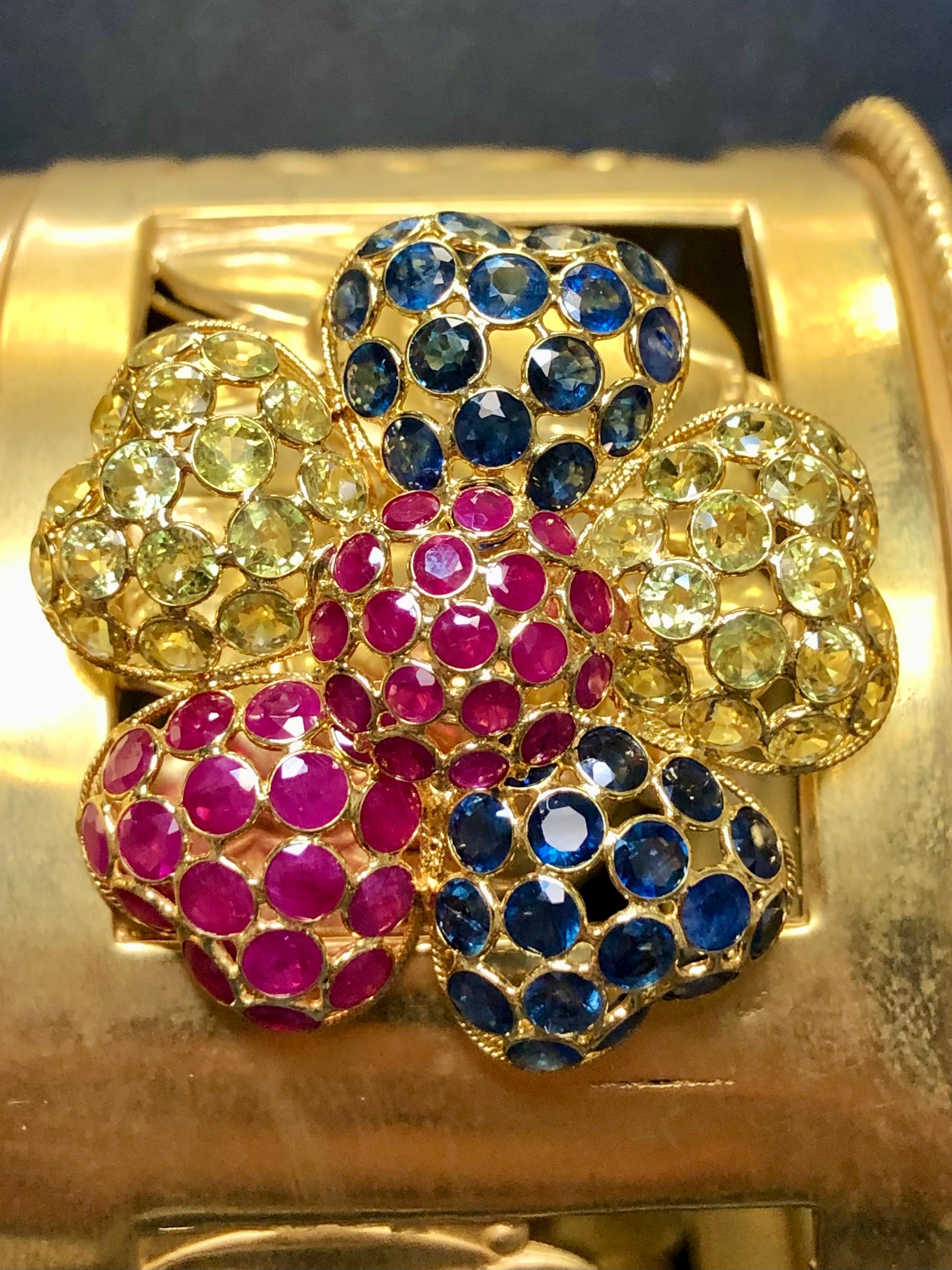 A lively brooch beautifully crafted in deep 18K yellow gold and bezel set with approximately 5.25cttw in rubies, 5.10cttw in blue sapphires and 5.10cttw in yellow sapphires. The beautiful mixture of colors really makes this piece