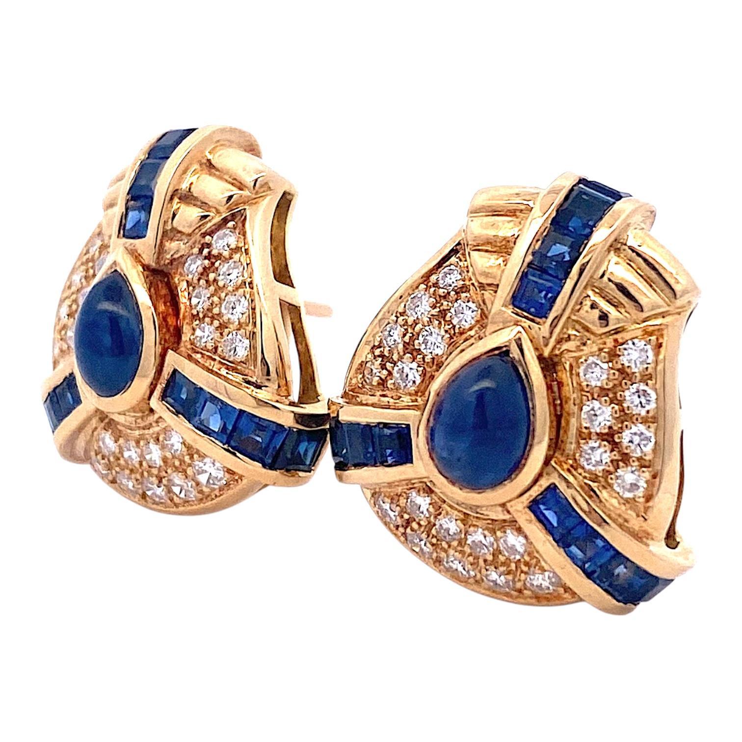 Crafted in 18K yellow gold, these earrings feature a striking cluster design with blue sapphires and round brilliant-cut diamonds. 18K post and 14K omega backs for extra security. 
2 pear shape cabochon cut sapphires: 2.44 ctw. 
24 square cut