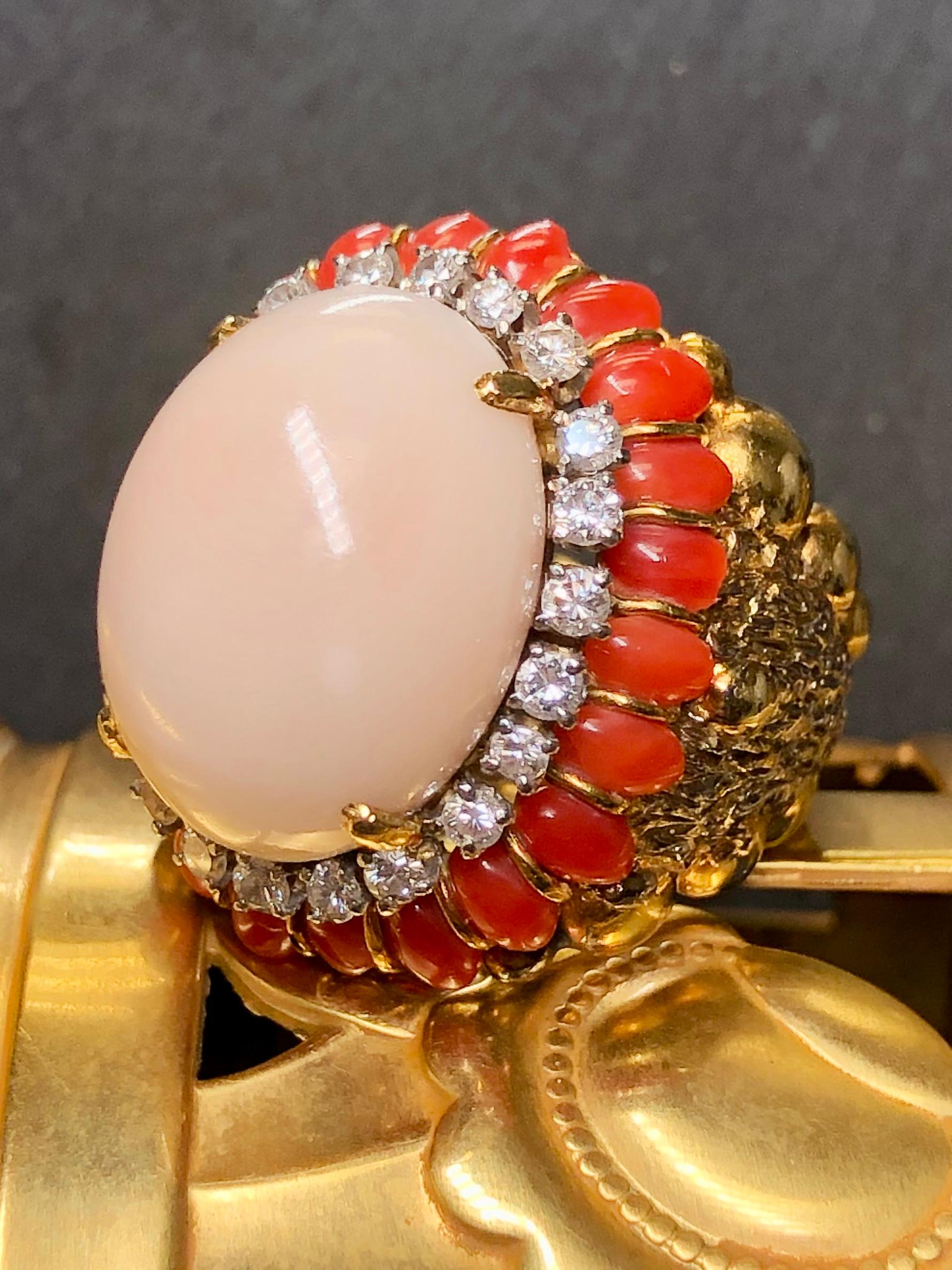 An impressive, large cocktail Ring c. the late 1960’s hand done in 18K yellow gold centered by an angel skin coral cabochon surrounded by smaller cabochons of deep red coral. Surrounding the center stone is approximately 1.10cttw in G-I color