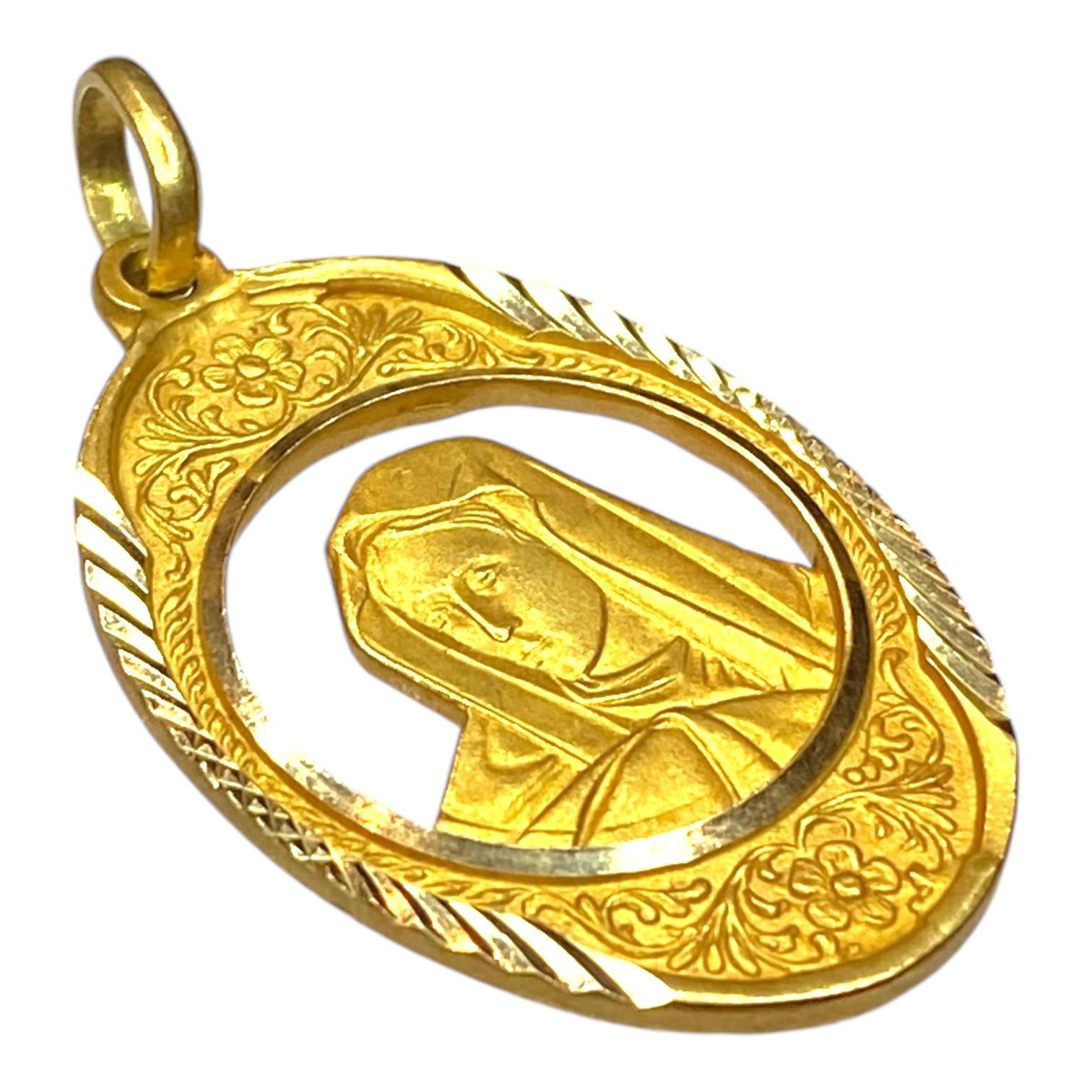Crafted in 18K yellow gold, this pendant features a detailed depiction of a veiled figure of the Madonna with a contemplative expression. 
The figure is framed by an ornate oval border with floral motifs and knife cut edges.
Bright polish and satin
