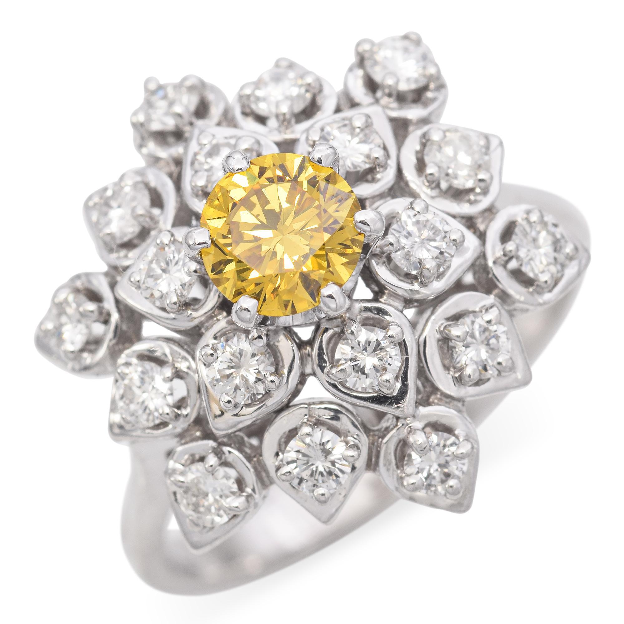Este anillo de cóctel está elaborado en oro blanco de 18 quilates. Presenta un vibrante diamante amarillo de talla redonda en el centro, con un peso aproximado de 0,57 quilates. Alrededor de la piedra central hay diamantes blancos talla redonda, con