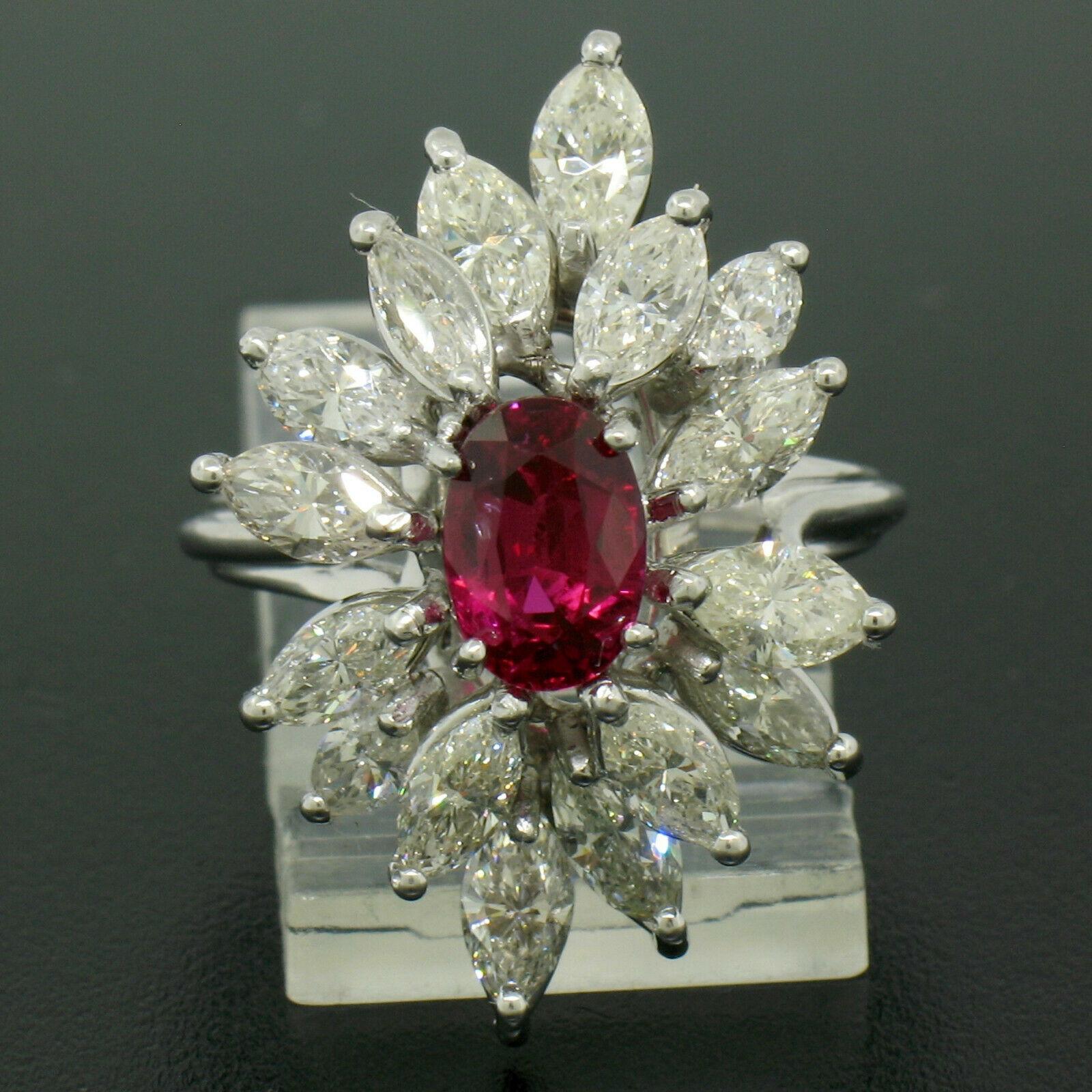 A truly breathtaking, GIA certified, genuine ruby ring crafted in solid 18k white gold featuring an oval cut ruby solitaire with an outstandingly rich and vivid red color. Marquise cut diamonds elegantly surround the center stone in a large cluster