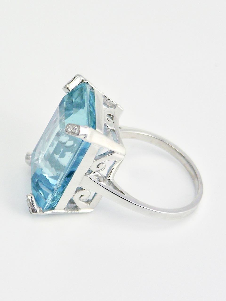 A white gold aquamarine and diamond ring consisting of an emerald cut aquamarine of 19cts of very good colour intensity and clarity, four claw set in 18k white gold with small brilliant cut diamonds mounted into the claws over a pierced and fretted