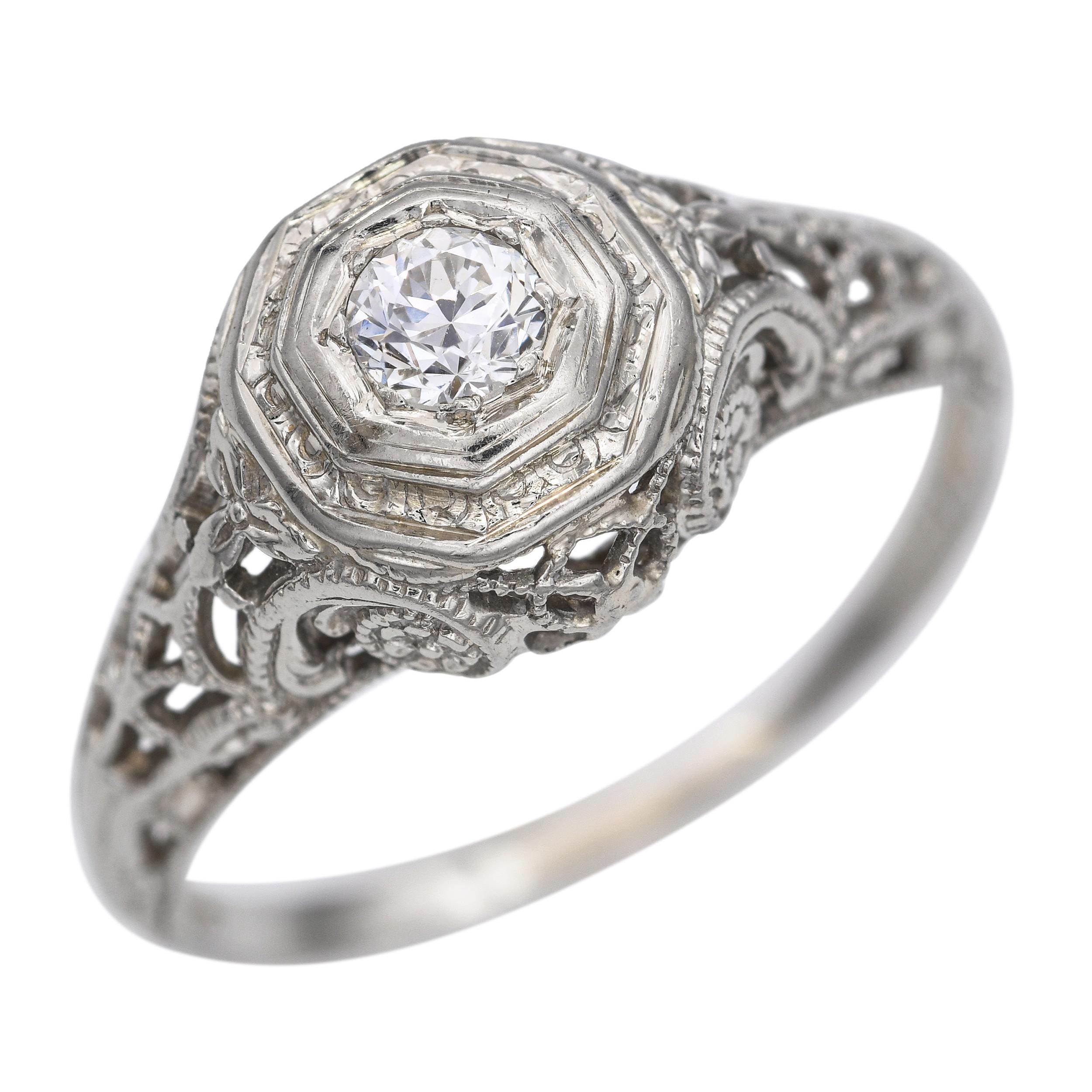 Este anillo vintage presenta un delicado diseño de filigrana elaborado en oro blanco de 18 quilates, centrado alrededor de un brillante diamante de 0,15 quilates. El patrón de filigrana calada resalta la artesanía de principios del siglo XX, con un