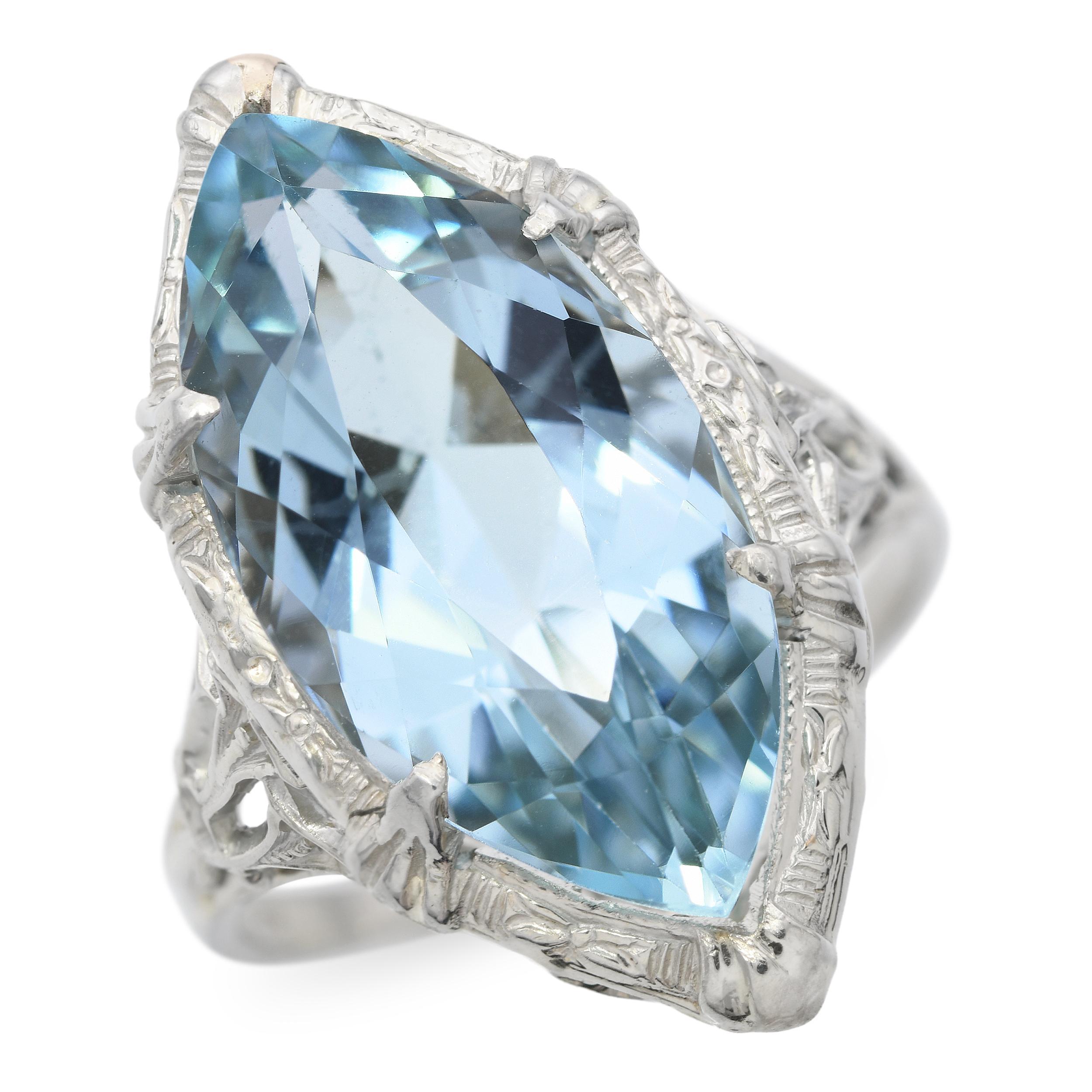 Dieser Vintage-Ring aus 18 Karat Weißgold zeigt in der Mitte einen auffälligen Aquamarin im Marquise-Schliff, der durch seine kühle blaue Brillanz und seine langgestreckte Eleganz besticht. Die filigranen Details, die den Stein umgeben,