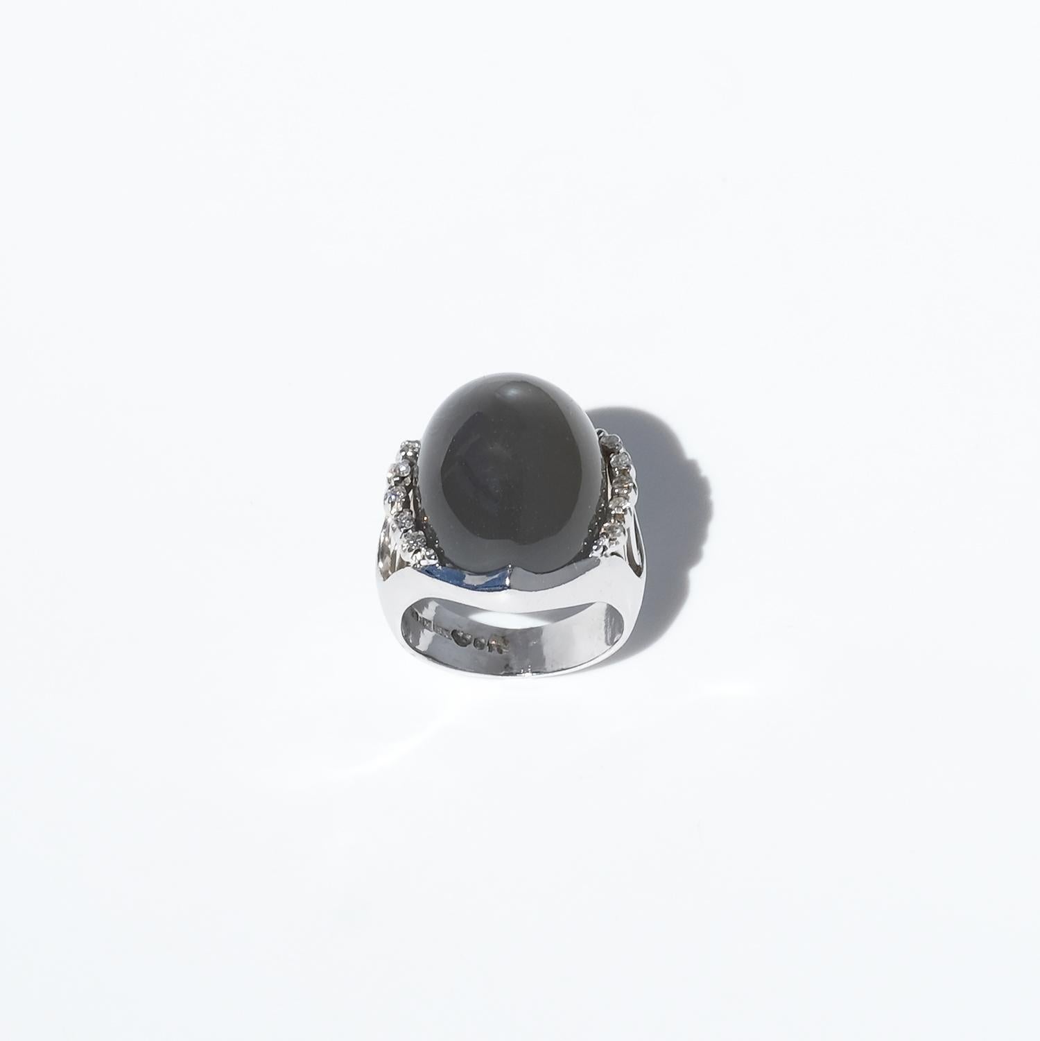 This vintage ring is crafted in 18-karat white gold, featuring a cabochon-cut moonstone with a smooth, polished surface. The gemstone has a rich gray-brown hue, exuding depth and warmth. Surrounding the moonstone, five octagonal-cut diamonds on each
