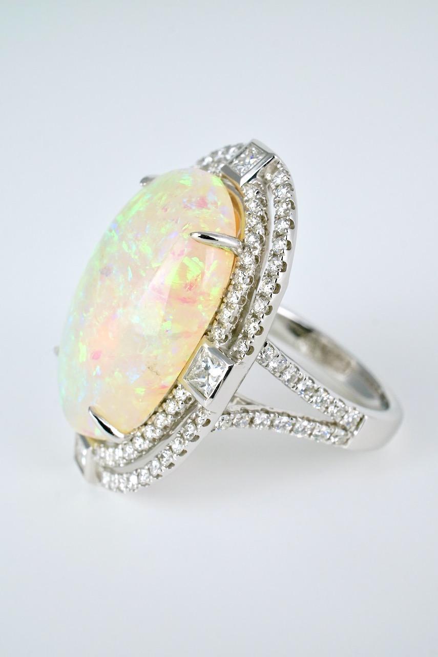 A vintage 18k white gold large oval opal and diamond ring featuring an oval crystal white opal cabochon four claw set in 18k white gold within a double halo of 76 round brilliant cut diamonds and with 4 princess cut diamonds set at the compass